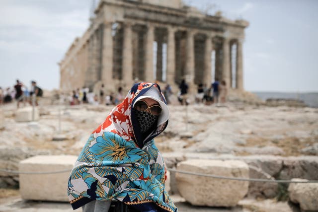 <p>A visitor wearing a hat and a scarf to shield her from the sun walks in front of the Parthenon temple atop the Acropolis hill during a heatwave, in Athens, Greece, 11 June 2024</p>