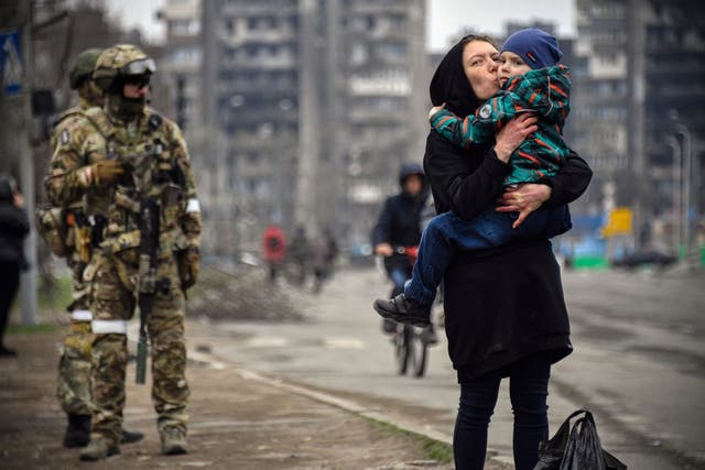 <p>A woman walks with a child next to Russian soldiers in Mariupol in April 2022 </p>