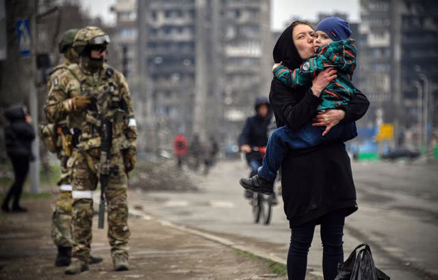 <p>A woman walks with a child next to Russian soldiers in Mariupol in April 2022 </p>