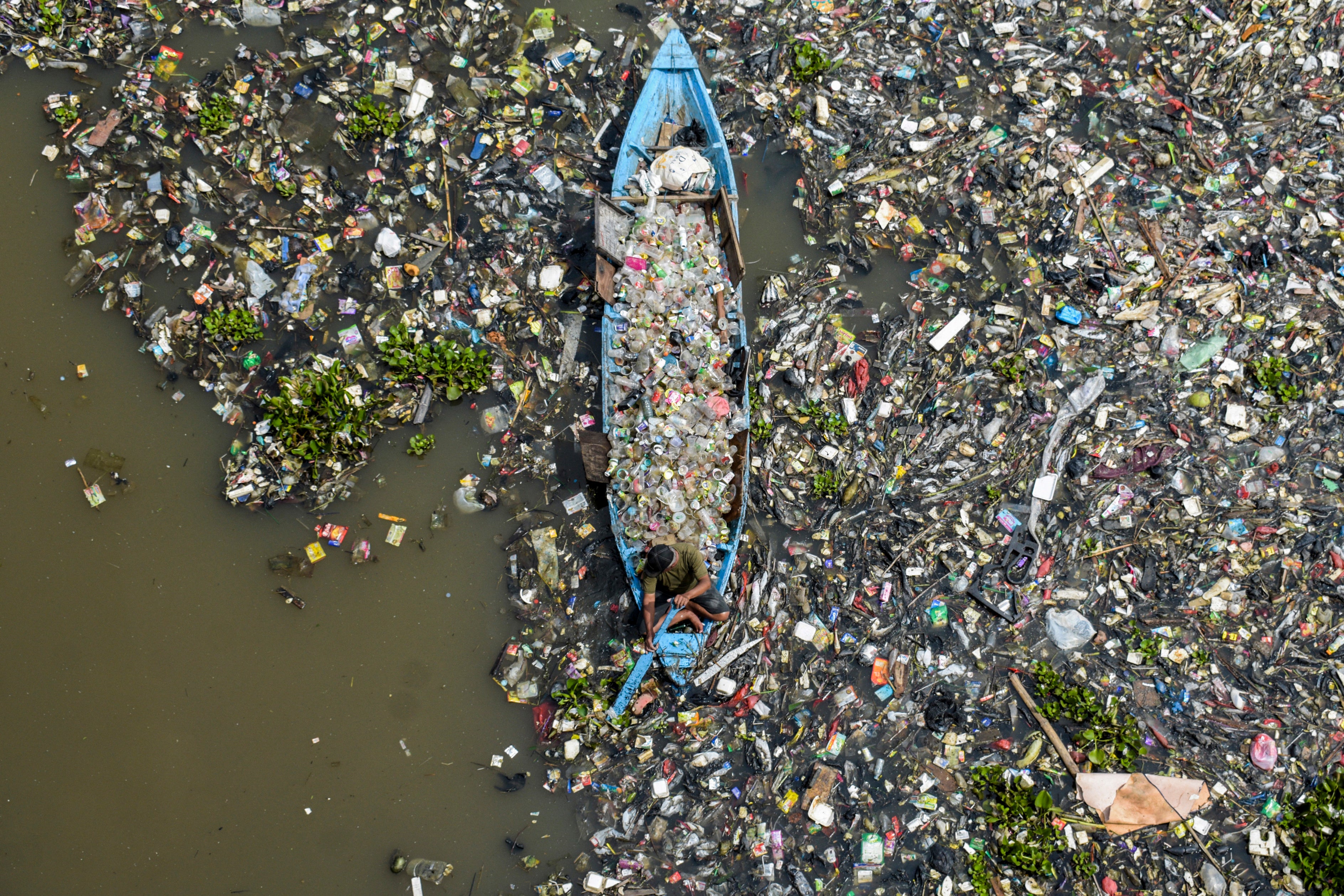 A boatman collects recyclable plastics from the heavily polluted Citarum River at Batujajar in Bandung, West Java, Indonesia