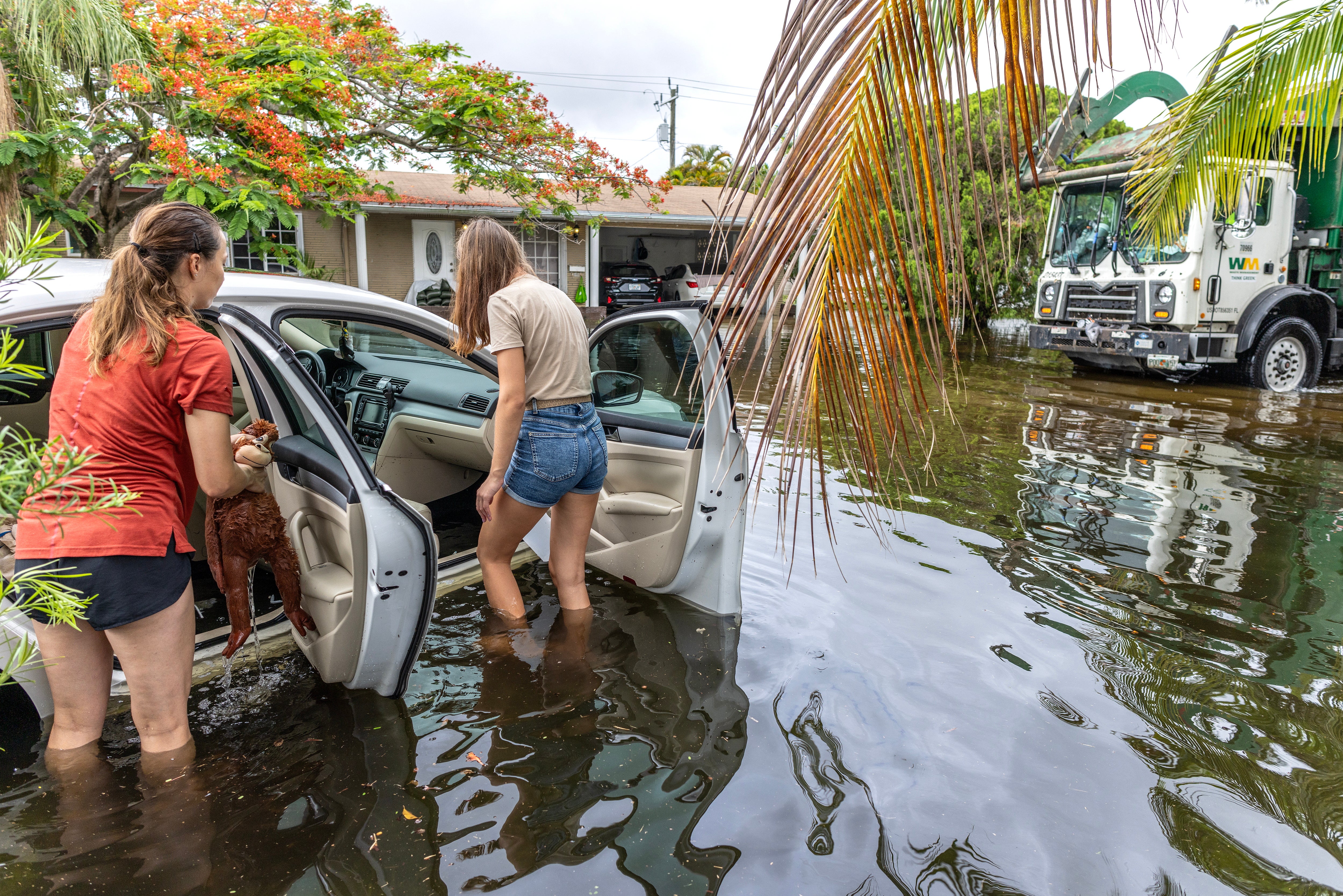 Two people stand next to a car in a flooded neighborhood in Hallandale Beach, Florida