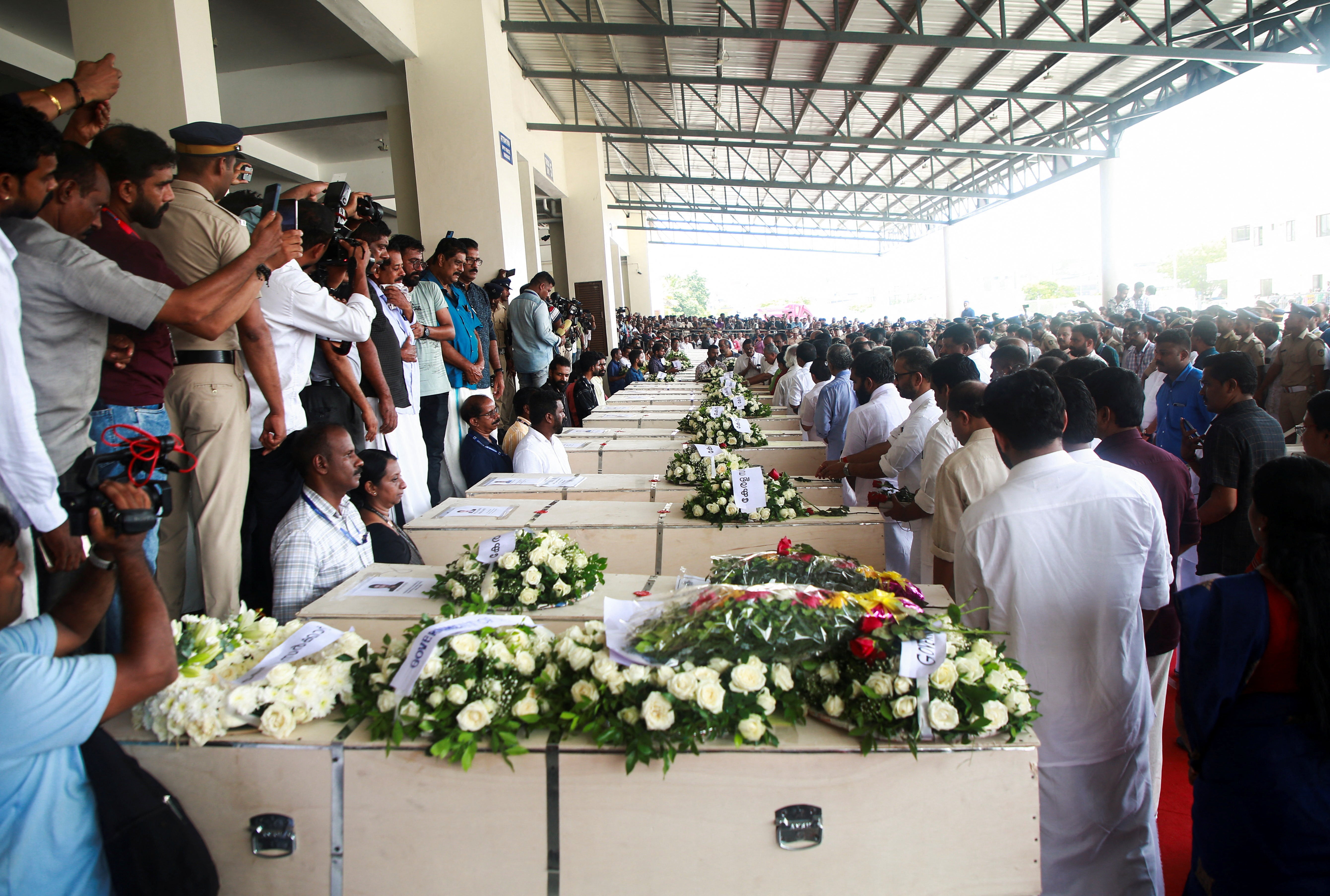 People gather around the coffins containing the bodies of people who died during a fire that broke out in a building housing foreign worker