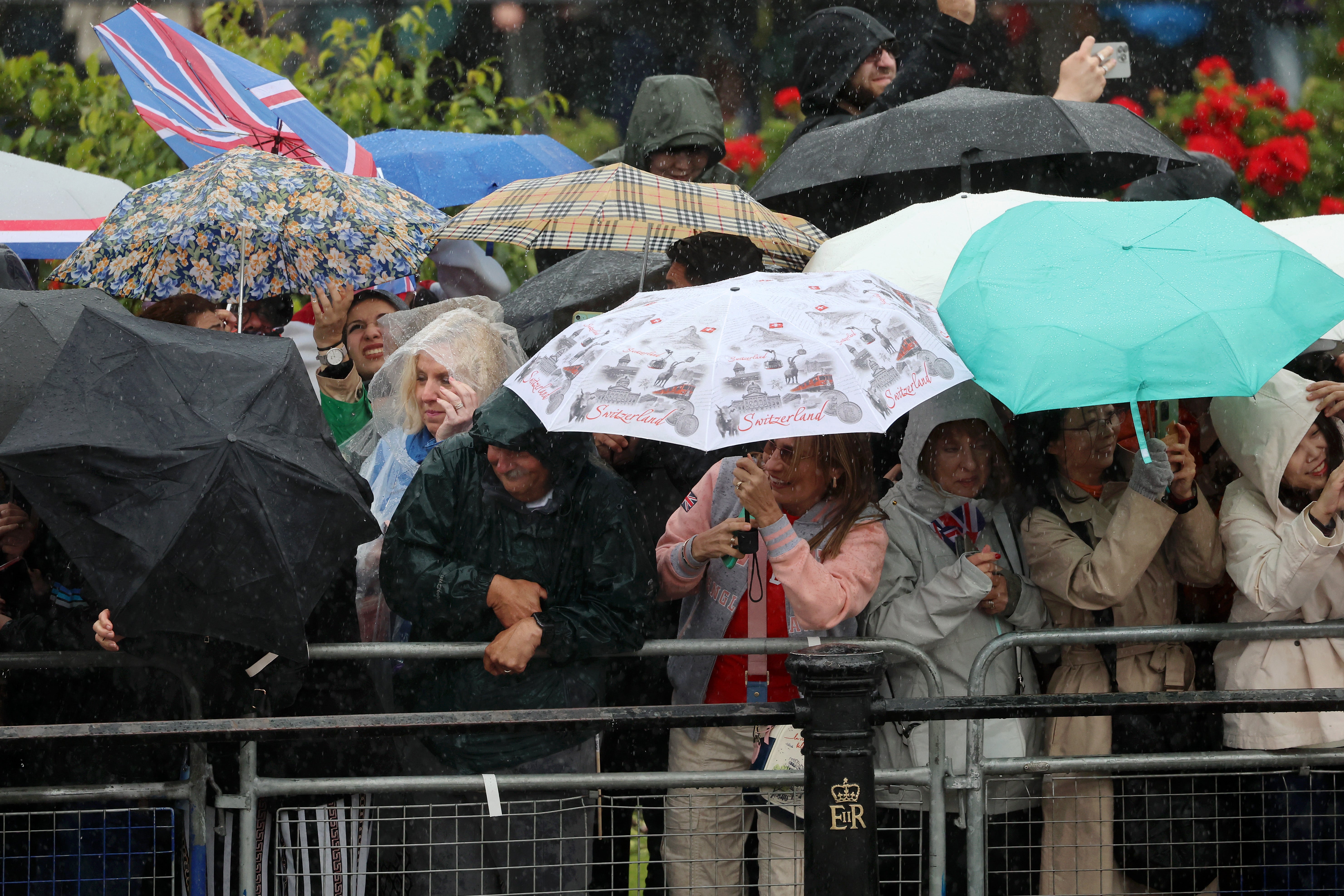 Crowds take cover under umbrellas as they wait for the balcony appearance