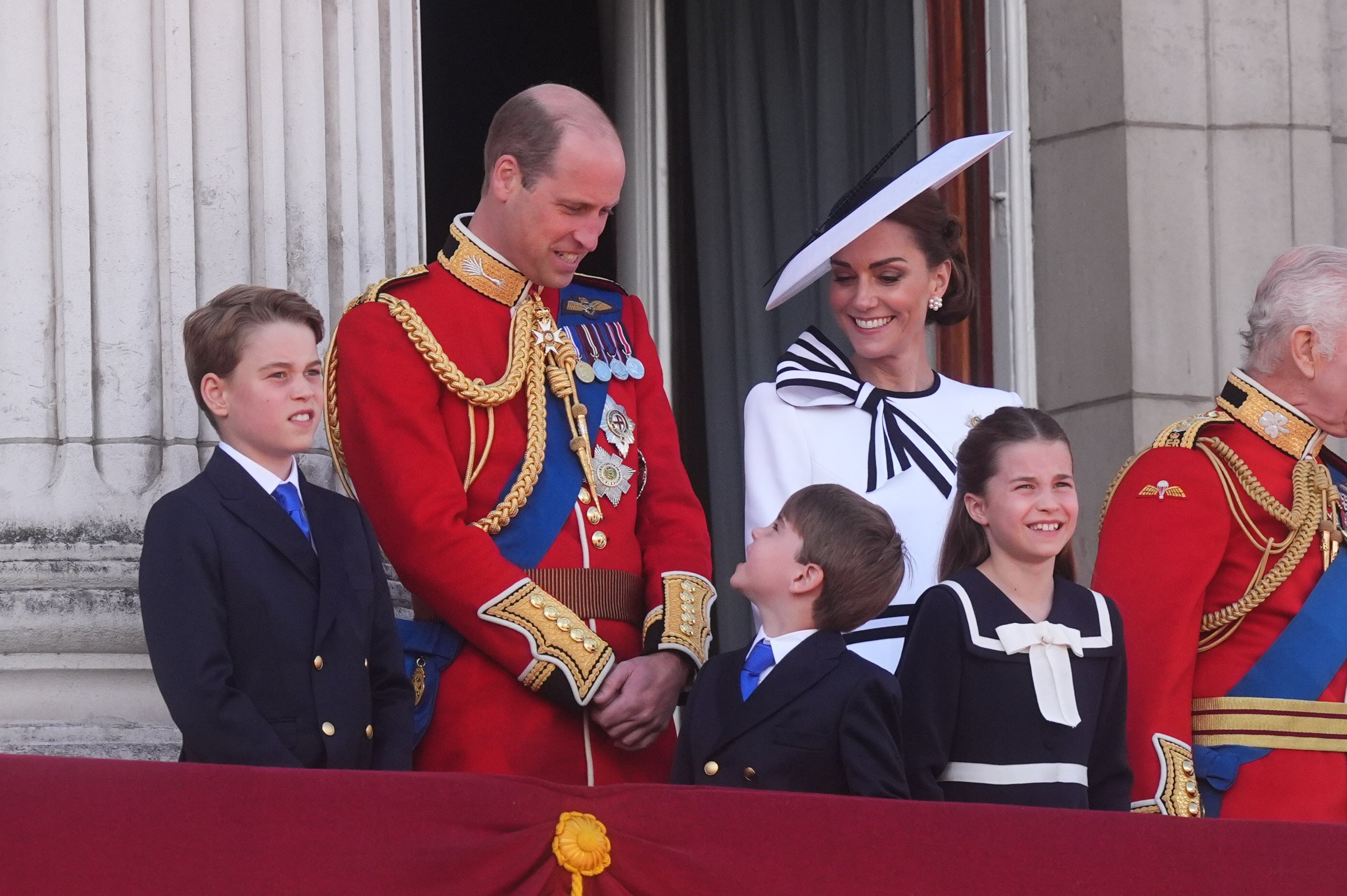Prince Louis looks up at his father as his mother the Princess of Wales smiles on the balcony of Buckingham Palace