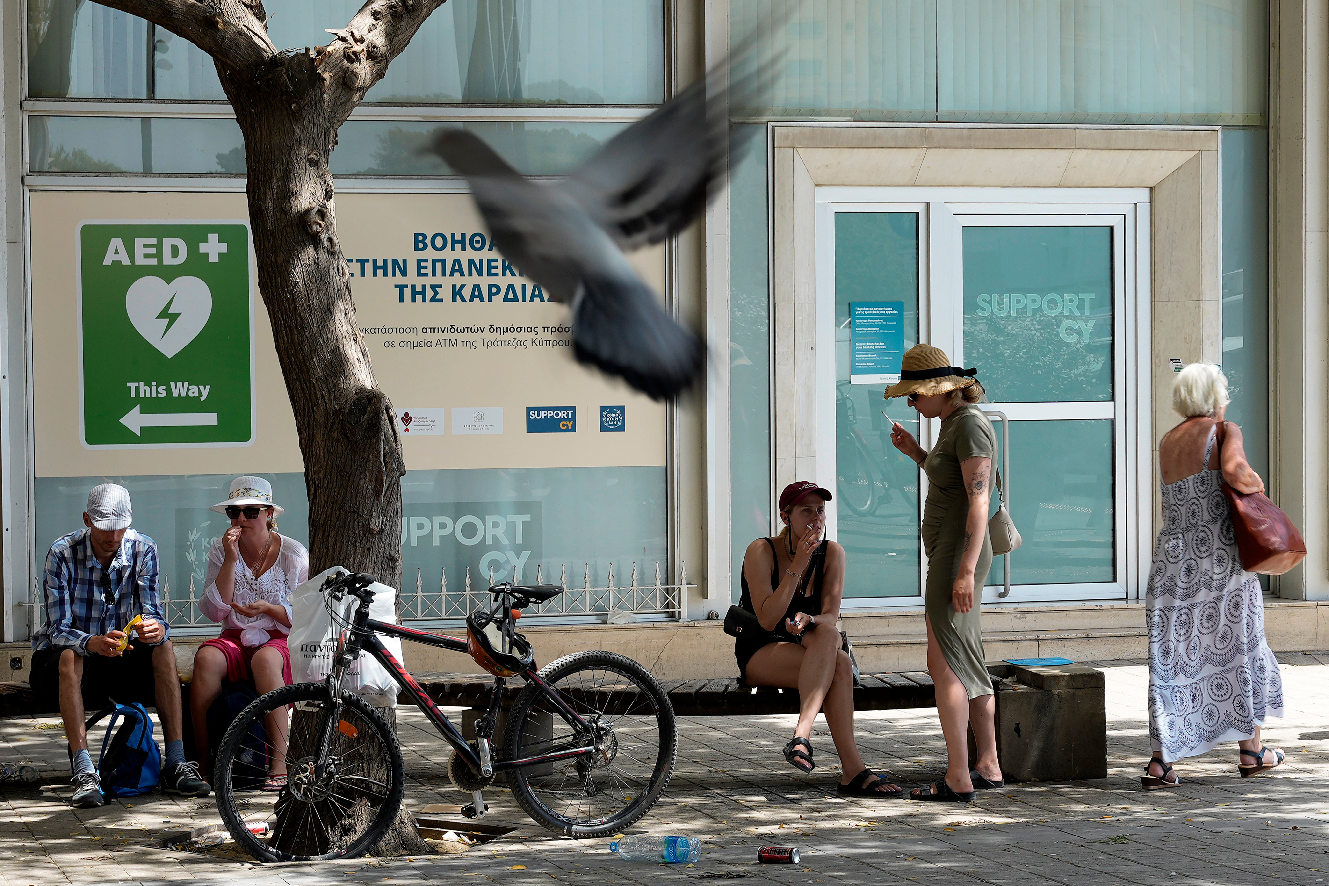 Tourists sit under a tree for shade amid hot weather at Eleftherias, Liberty, square in central capital Nicosia, Cyprus