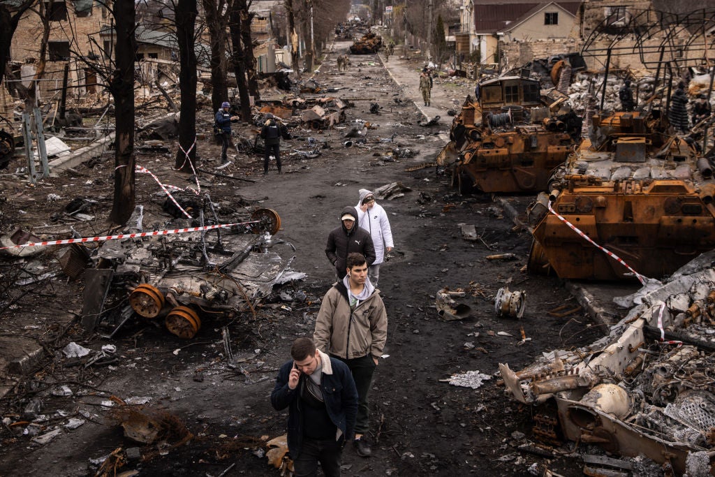 People walk through debris and destroyed Russian military vehicles on a street in Bucha, where Mykhed’s parents had been living at the start of the invasion