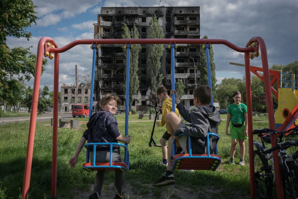 Children play on the swings outside a burnt-out building destroyed by a Russian missile strike in Borodyanka, Kyiv Oblast