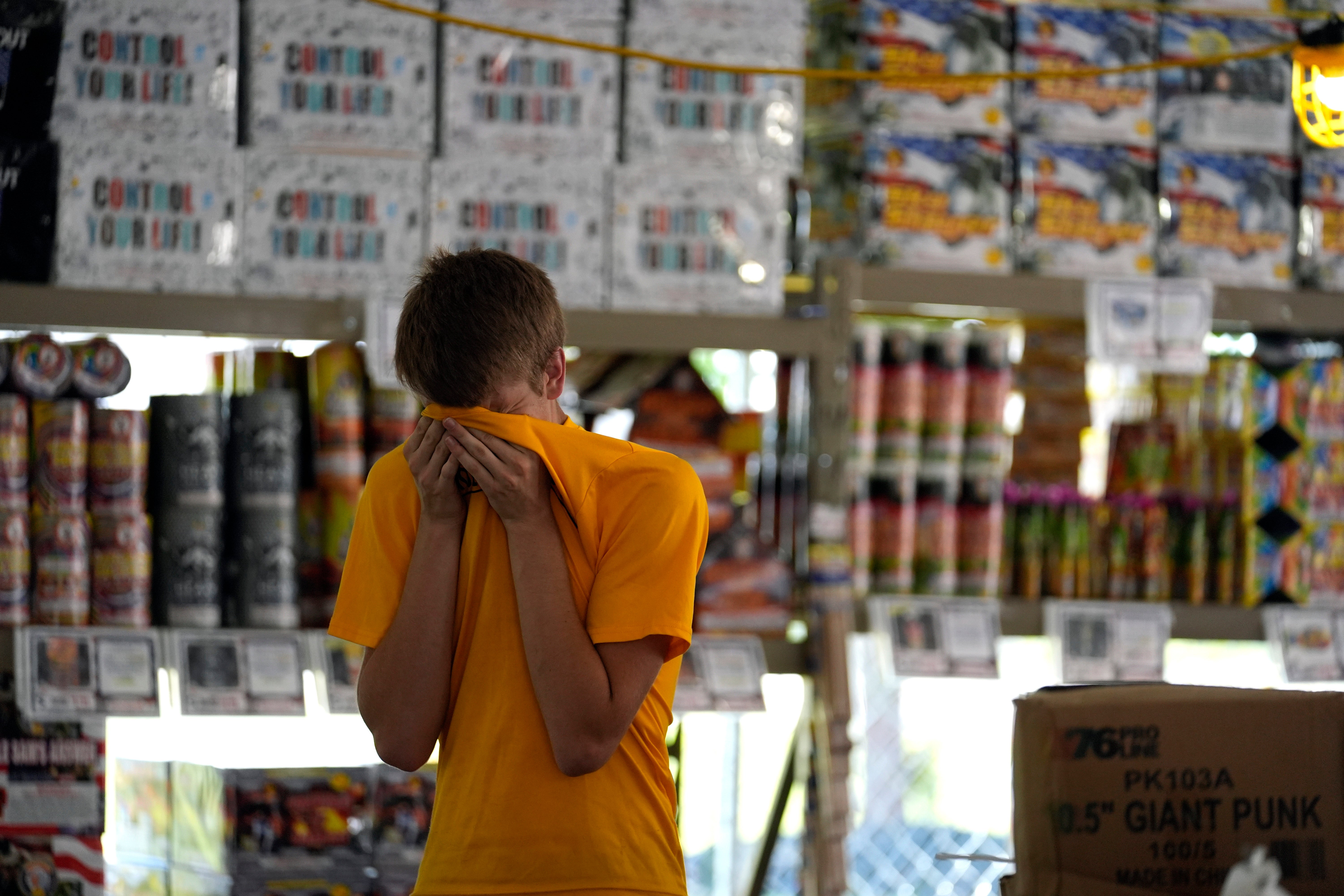 Hunter Van Dyne pauses to wipe sweat from his forehead inside a hot fireworks tent as he works to set up for the opening of Powder Monkey Fireworks, in Weldon Spring, Mo., Monday, June 17, 2024