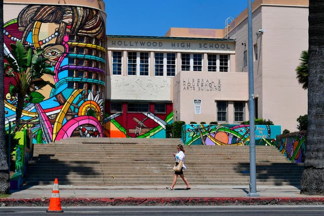 <p>A pedestrian walks past a quiet scene in front of Hollywood High School in Hollywood, California on September 3, 2020</p>
