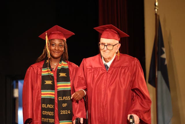 <p>Harlan Olson, 101, walks across the stage at Denfeld High School with senior Grace Nonnemacher</p>