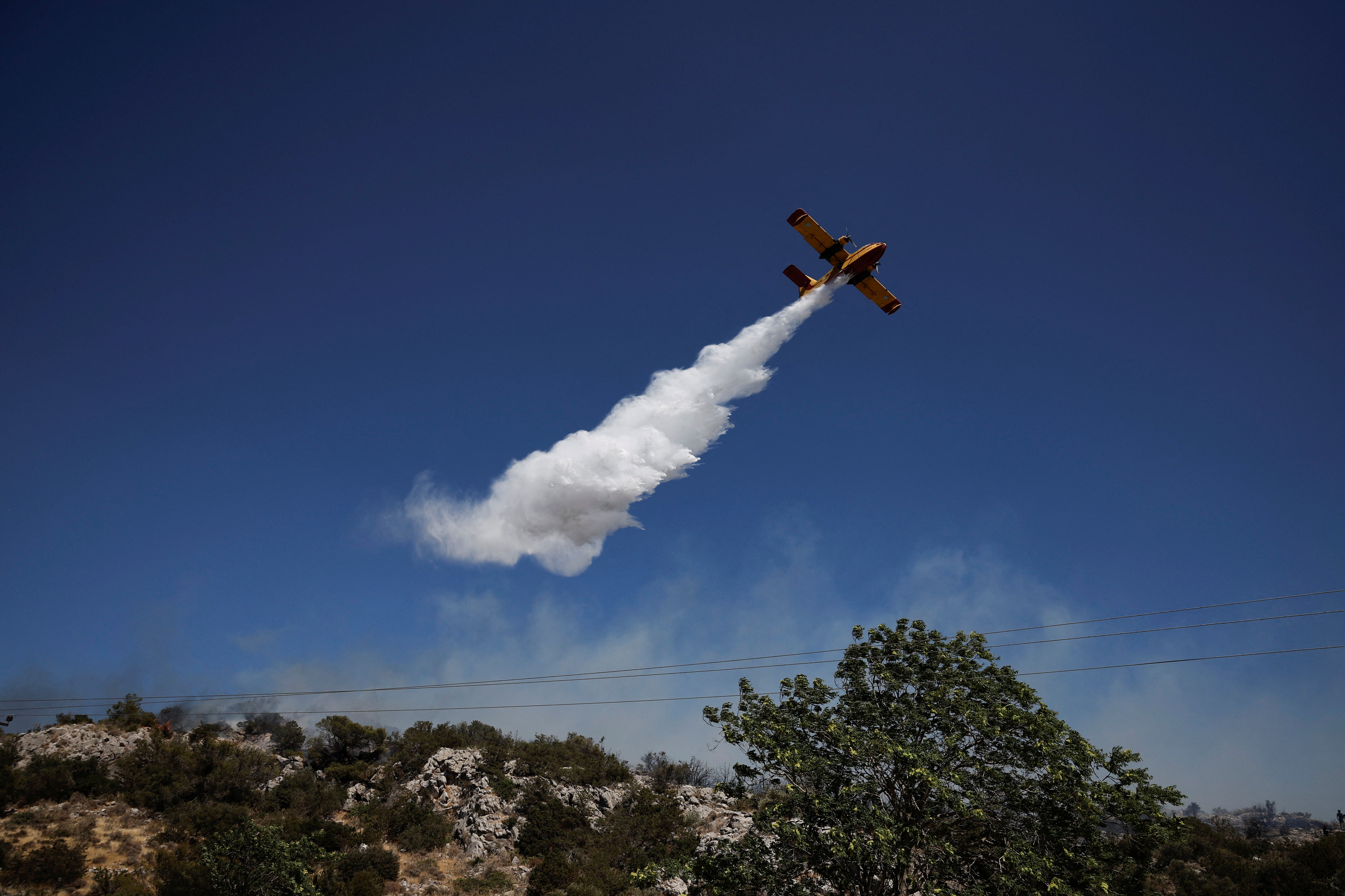 A plane drops water as firefighters try to extinguish a wildfire near the town of Koropi, Greece