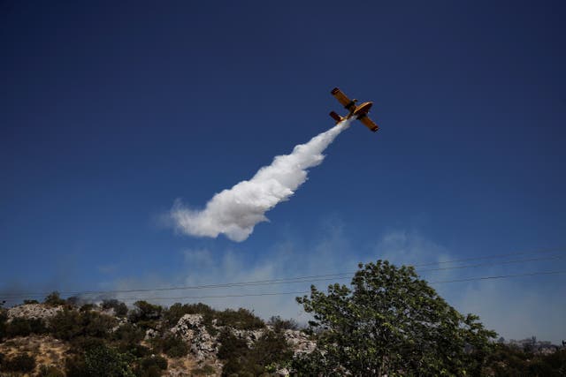 <p>A plane drops water as firefighters try to extinguish a wildfire near the town of Koropi, Greece</p>