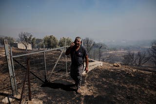 A man walks in an area burned during a wildfire in Kitsi near the town of Koropi in Greece on Wednesday