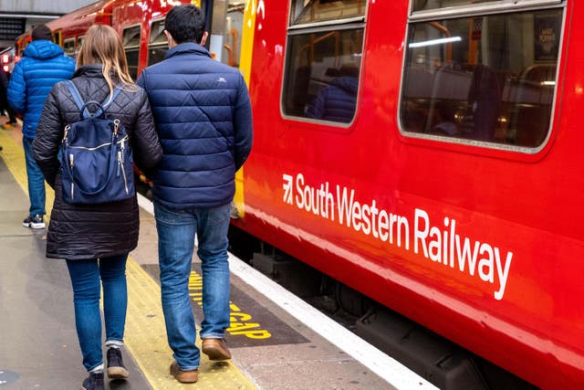 <p>A man and woman walk past a South Western Railway train at a station</p>