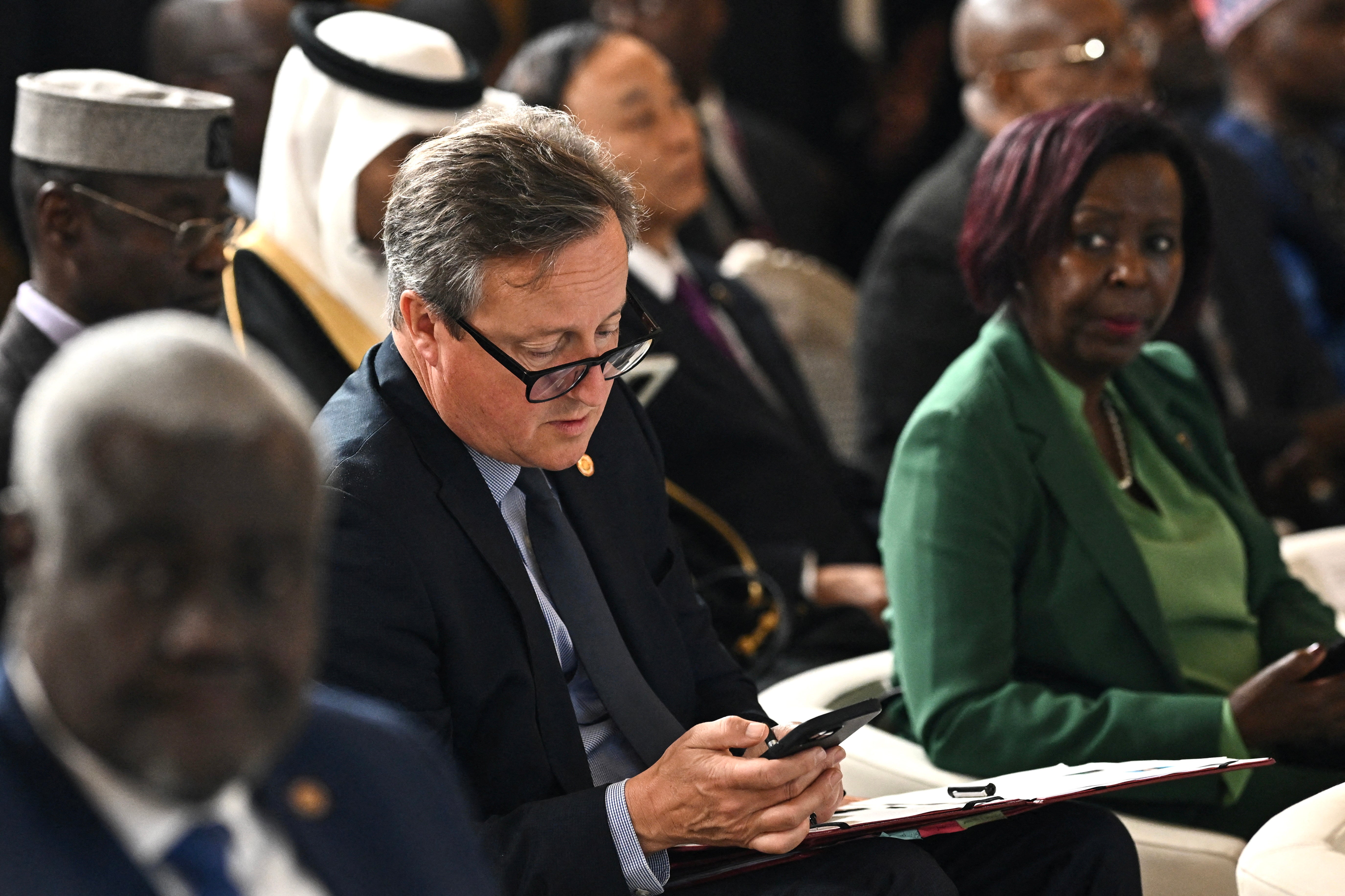 Foreign Secretary David Cameron (C) looks on his mobile phone as he attends the Global Forum for Vaccine Sovereignty and Innovation at the French Foreign Ministry, the Quai d'Orsay, in Paris, France