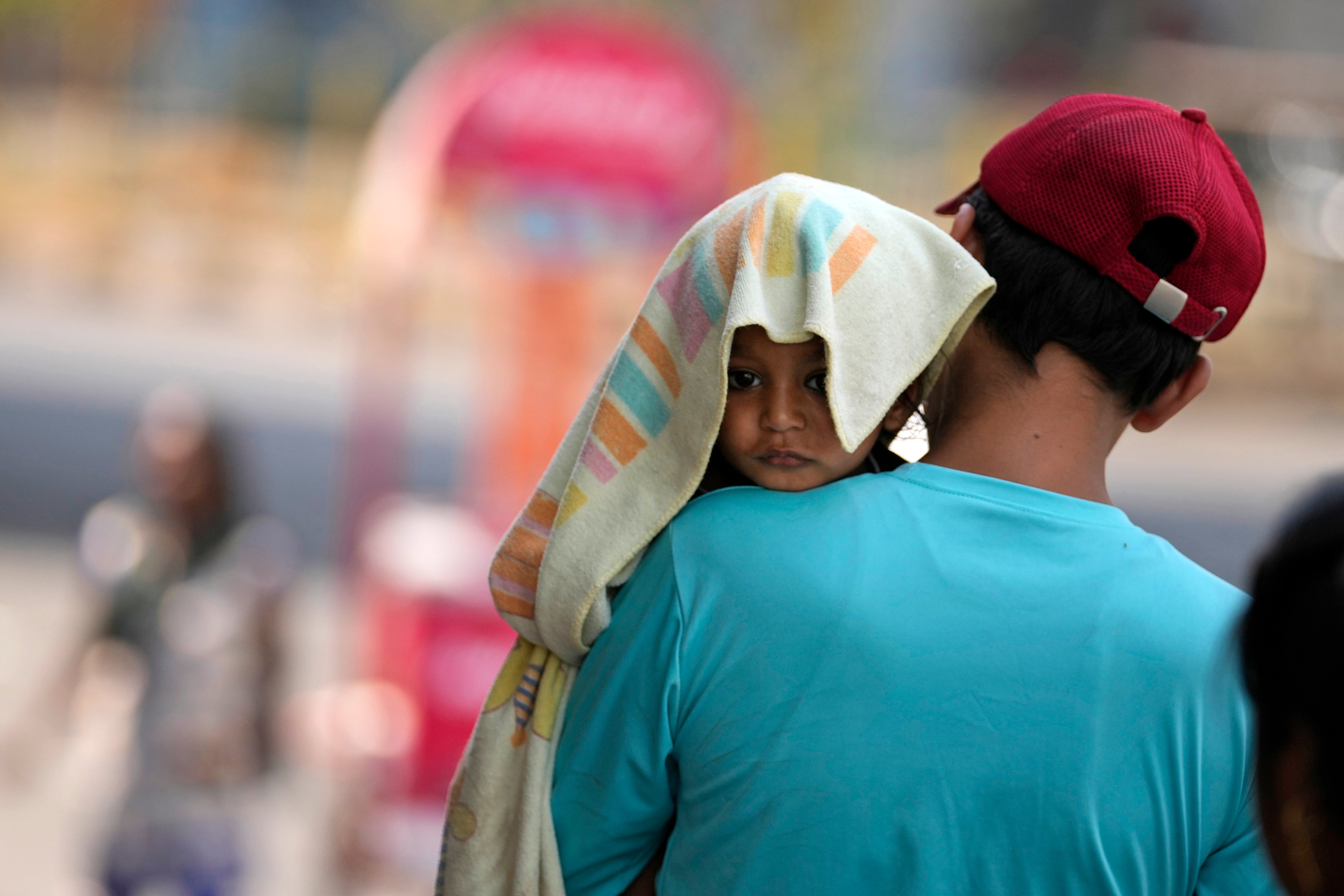 A man carries a child, head covered with a towel to protect from the heat, in Jammu, India