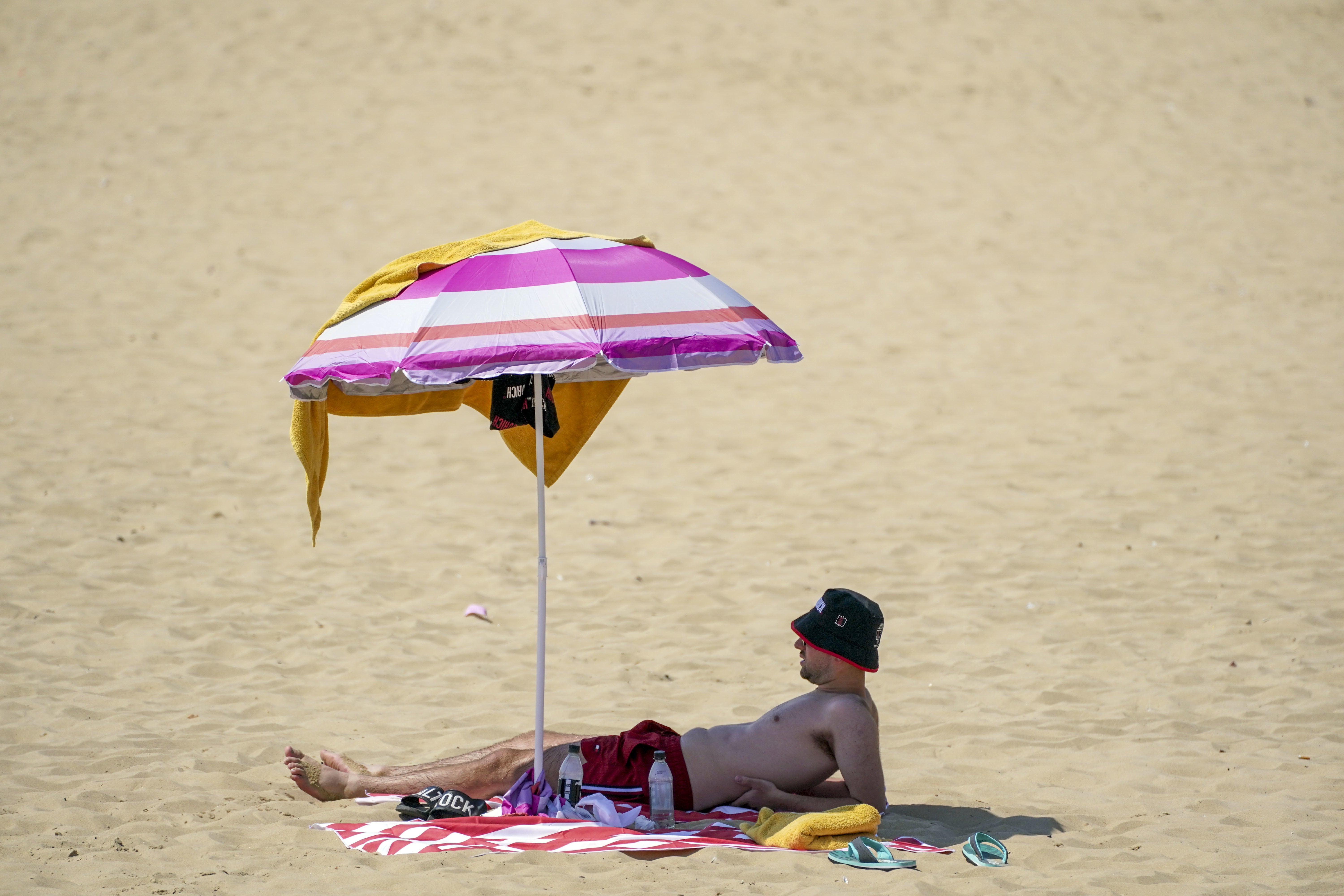 A man shelters under a umbrella on the beach in Bournemouth