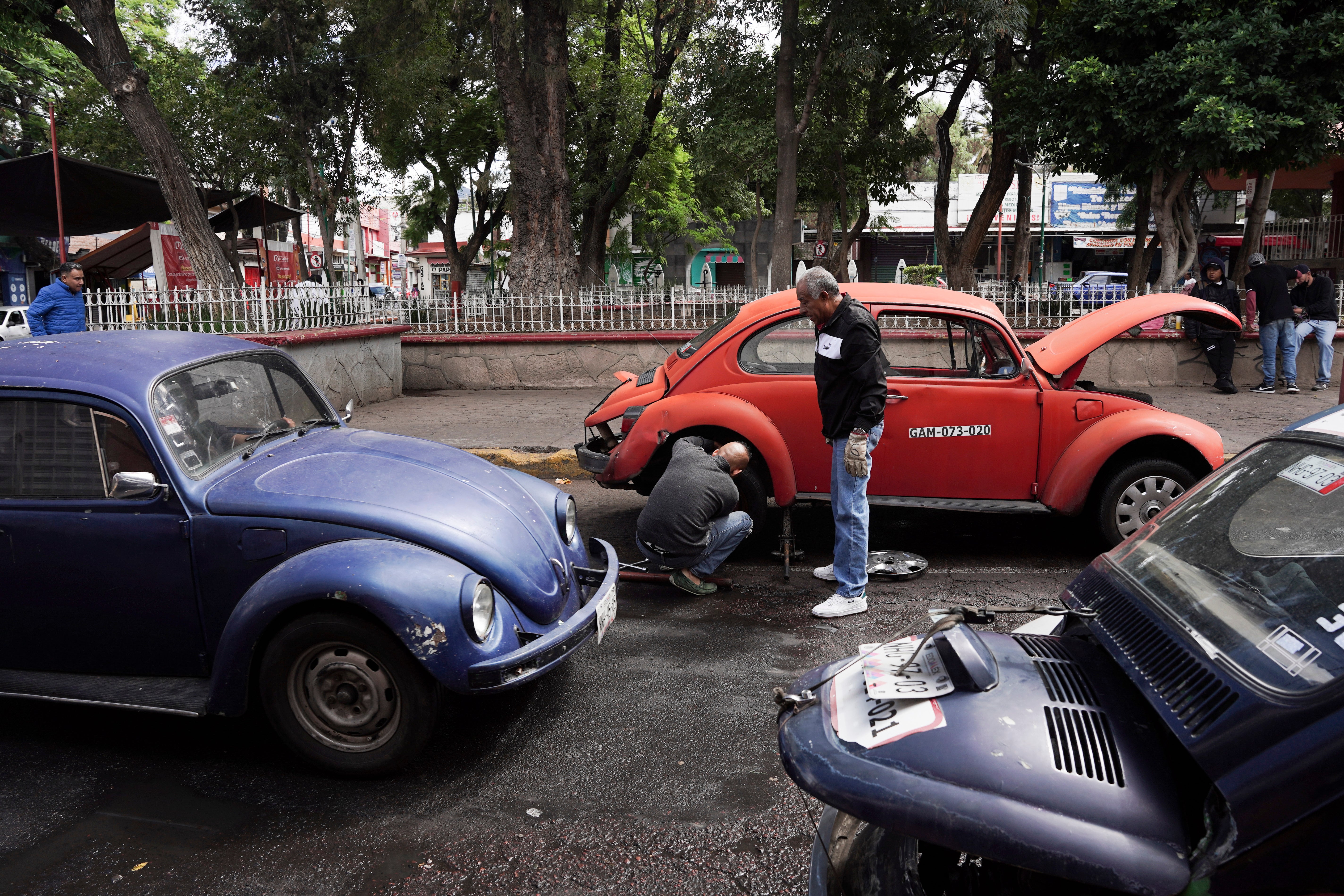 Volkswagen Beetle taxi drivers change a flat tire in the Cuautepec neighborhood of Mexico City, Friday, June 21, 2024