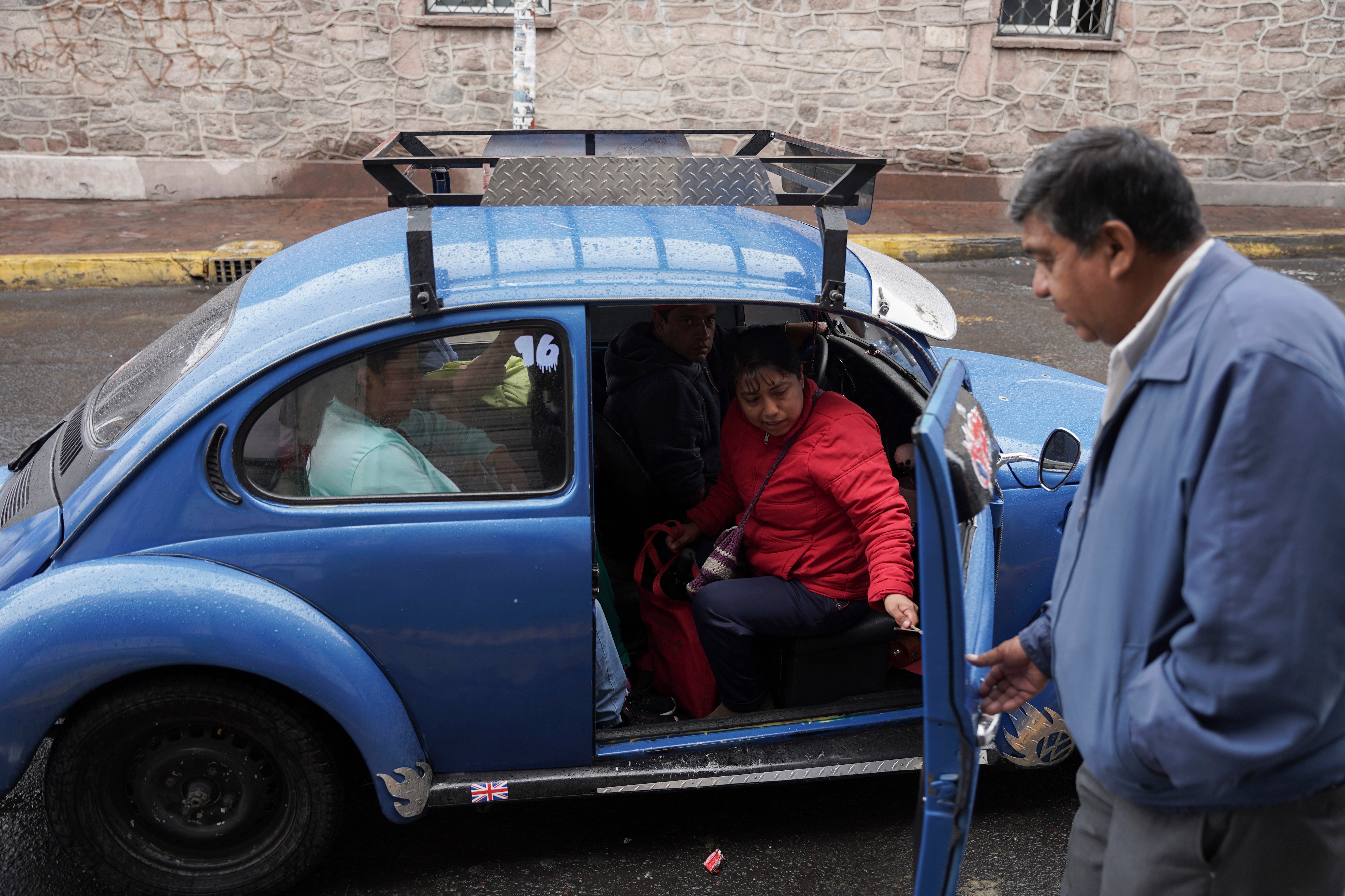 Taxi rank manager Rafael Ortega helps passengers into a Volkswagen Beetle in the Cuautepec neighborhood of Mexico City