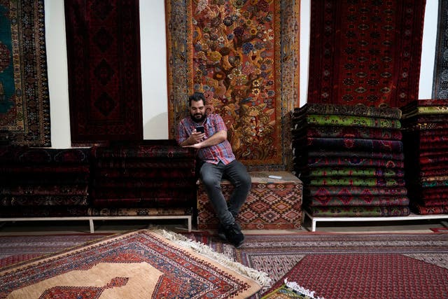 <p>A salesman works on his cell phone at a carpet shop in the old main bazaar of Tehran, Iran, Thursday, June 13, 2024</p>