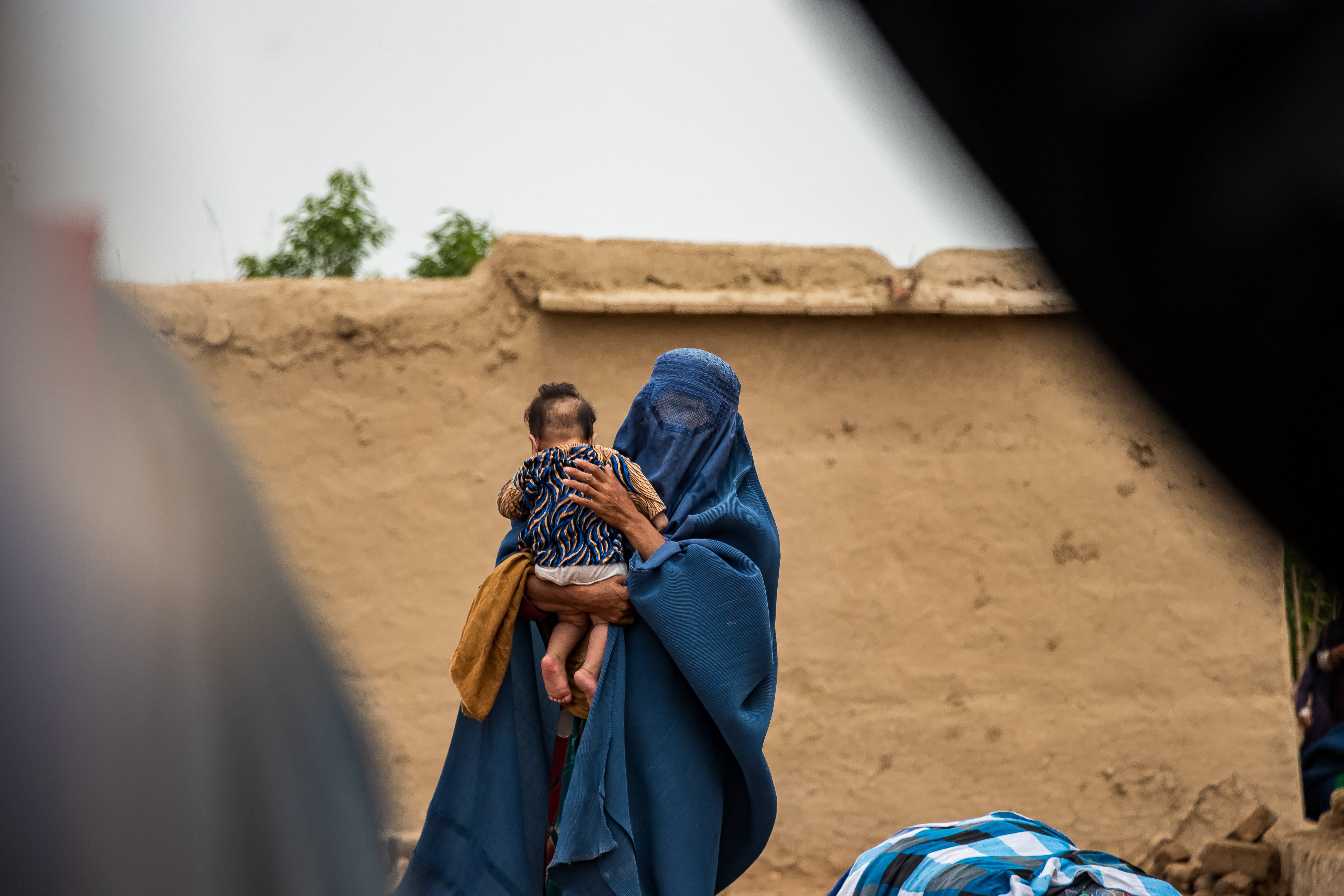 <p>A woman holds her baby in their house after flash floods devastated villages in Baghlan, Afghanistan, on 17 May 2024</p>