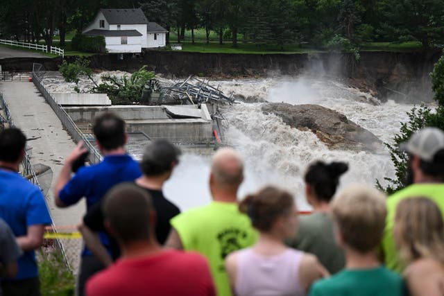 <p>A crowd watches a home on the brink of collapse near the Rapidan Dam in Minnesota. Severe flooding and debris caused the dam to partially fail on Monday</p>