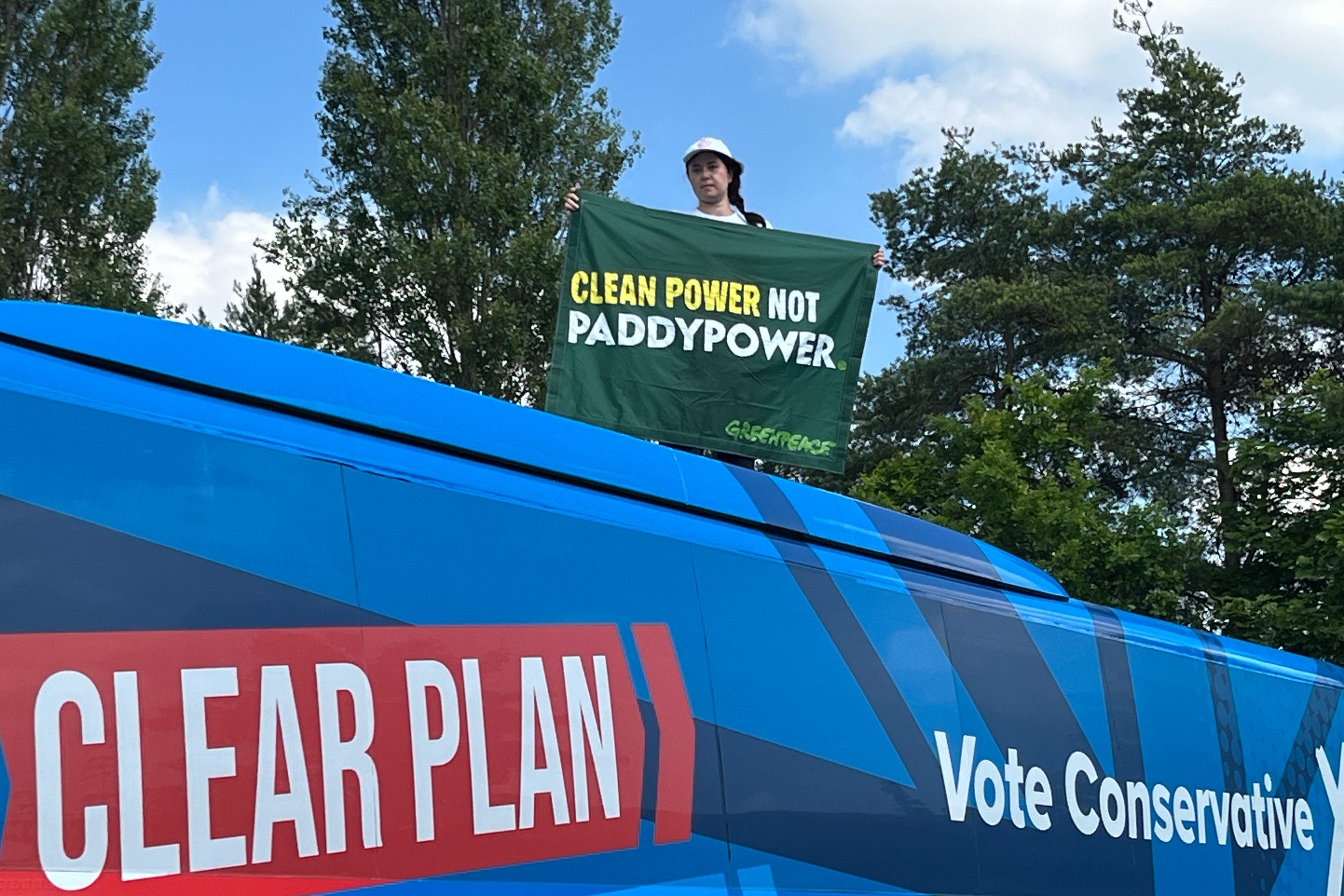 A Greenpeace protester unfurls a banner saying ‘Clean Power Not Paddy Power’ on top of the Conservative election battlebus (Kristian Buus/Greenpeace UK/PA)