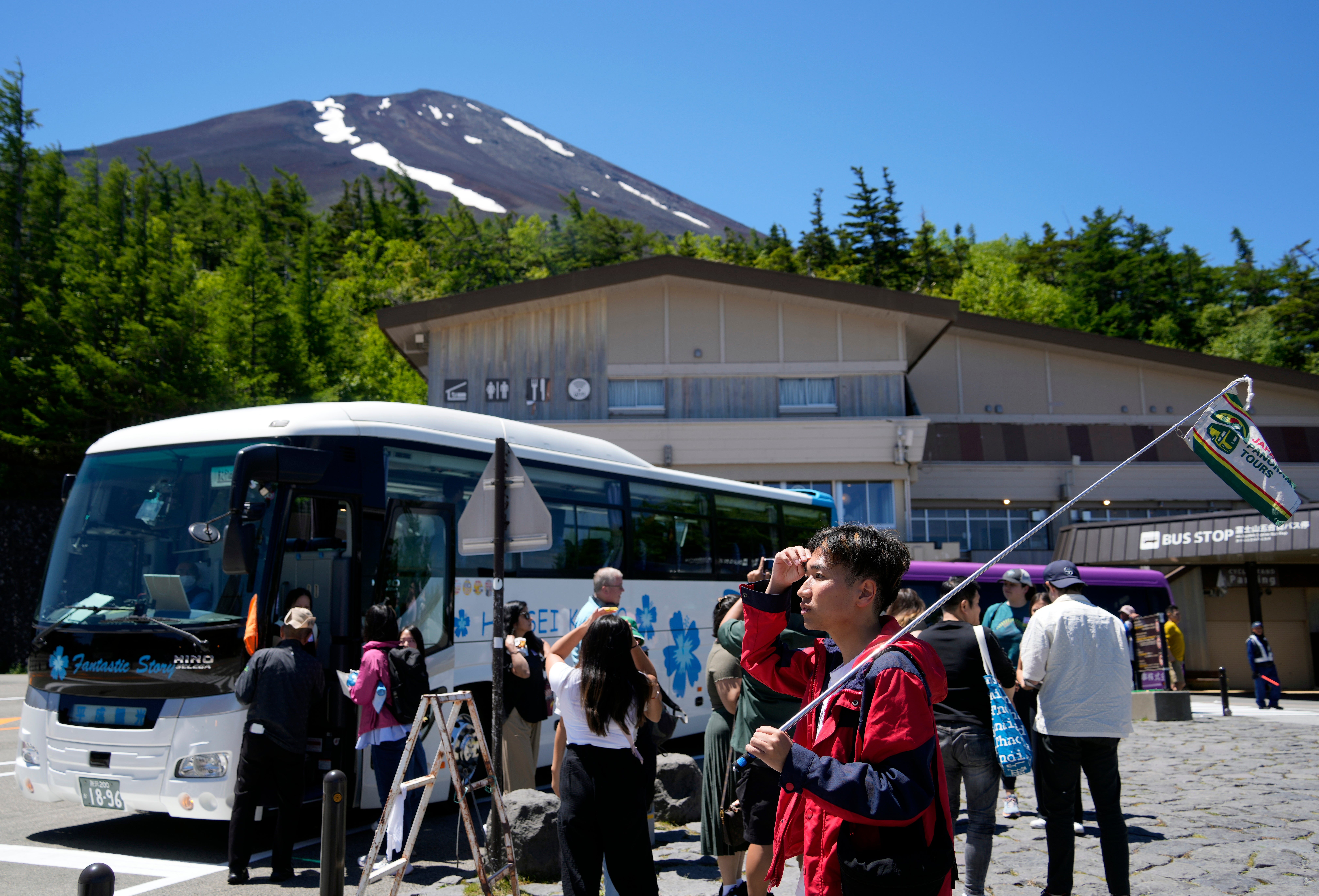 A tour conductor holds a flag at a Mount Fuji station as the summit is seen in the background in Yamanashi prefecture on 19 June 2024
