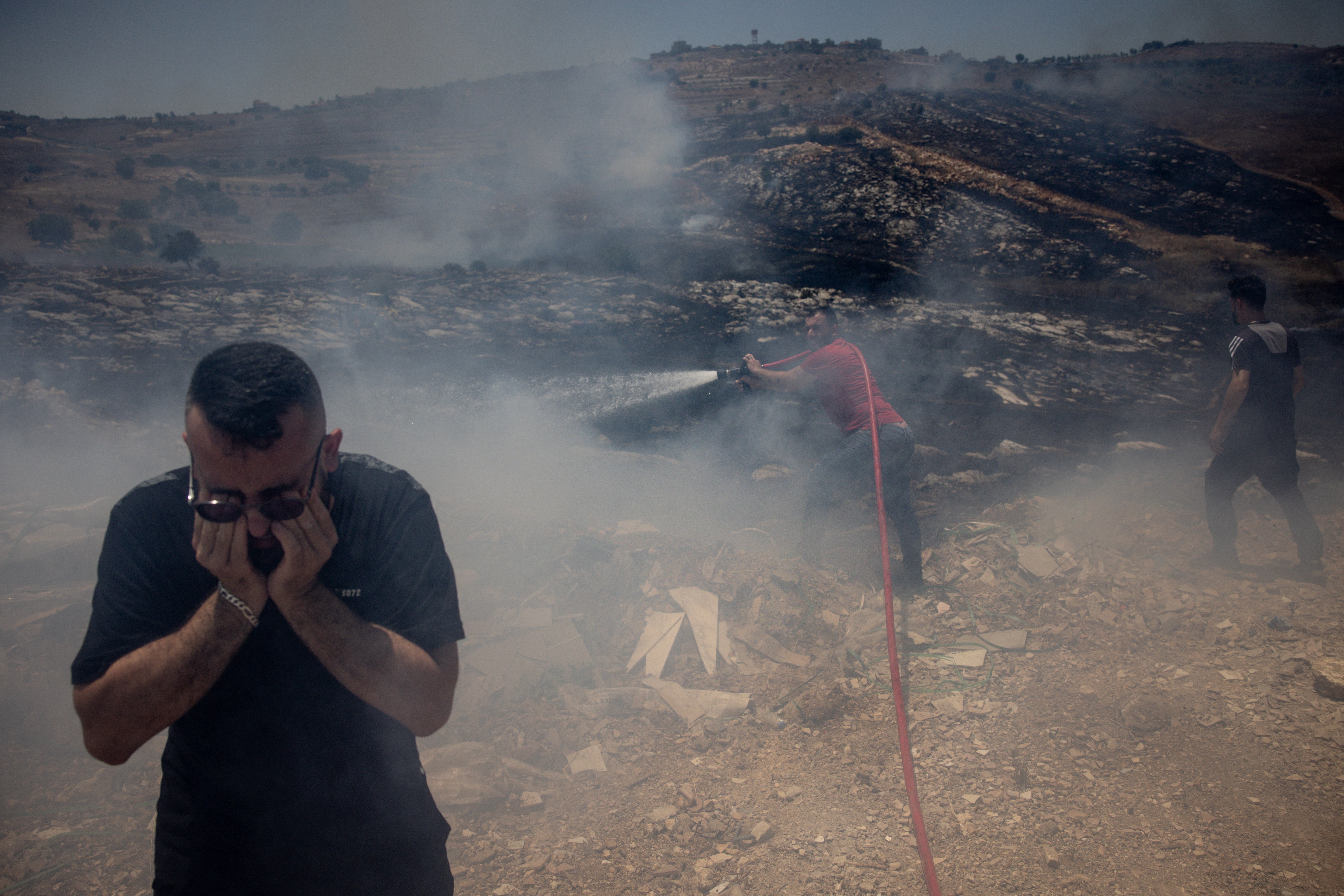 A man protects his eyes from smoke as civilians try to put out fires caused by multiple Israeli strikes that hit targets next to the main road in Bint Jbeil, Lebanon