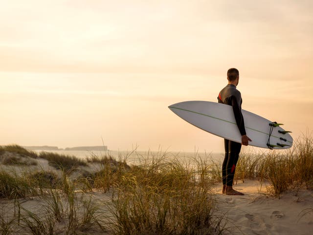 <p>A surfer with his surfboard at the dunes looking to the waves</p>