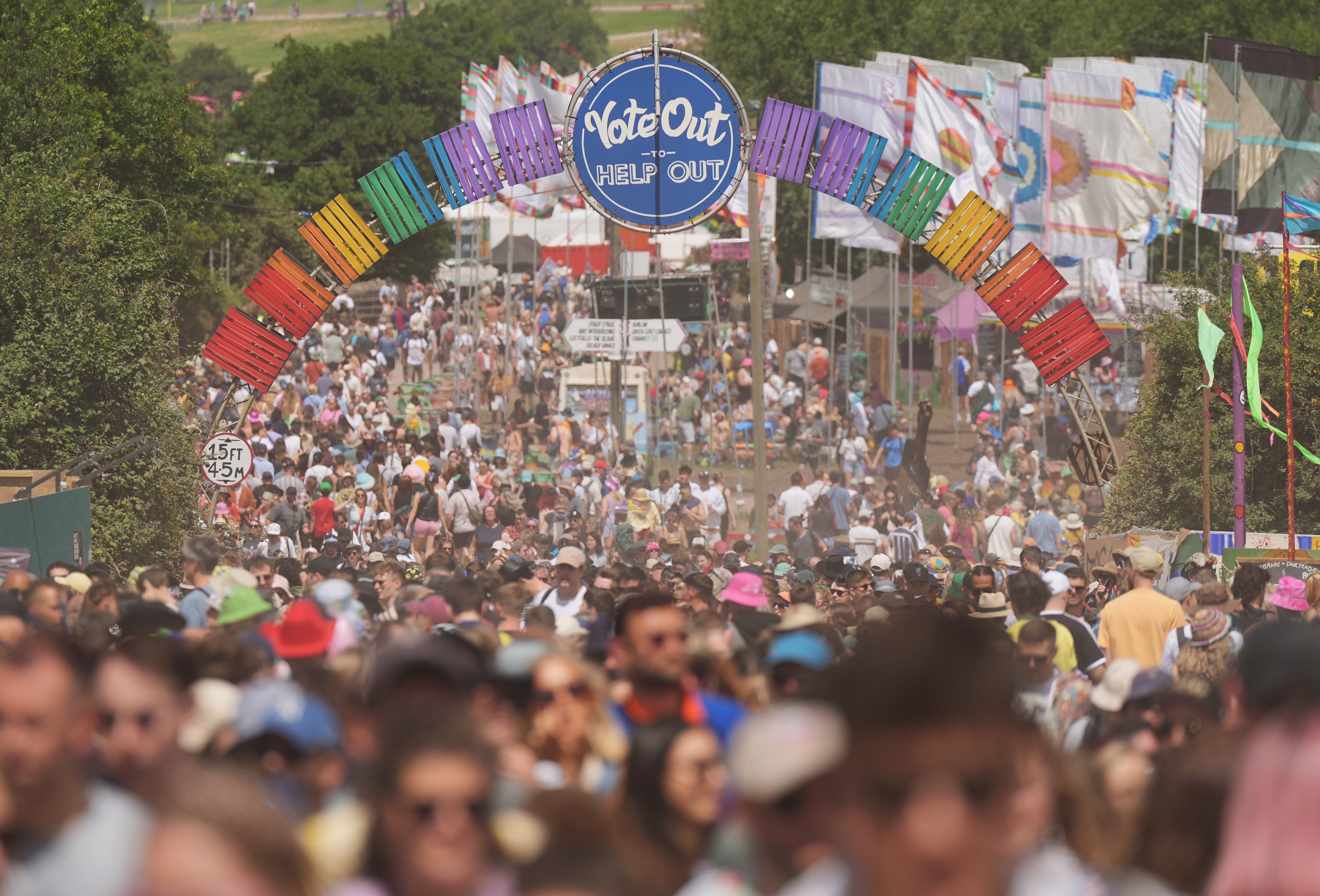 Festival-goers walk beneath a ‘Vote Out to Help Out’ sign at Glastonbury Festival 2024 – held while General Election campaigns continue outside the Worthy Farm boundary (Yui Mok/PA)