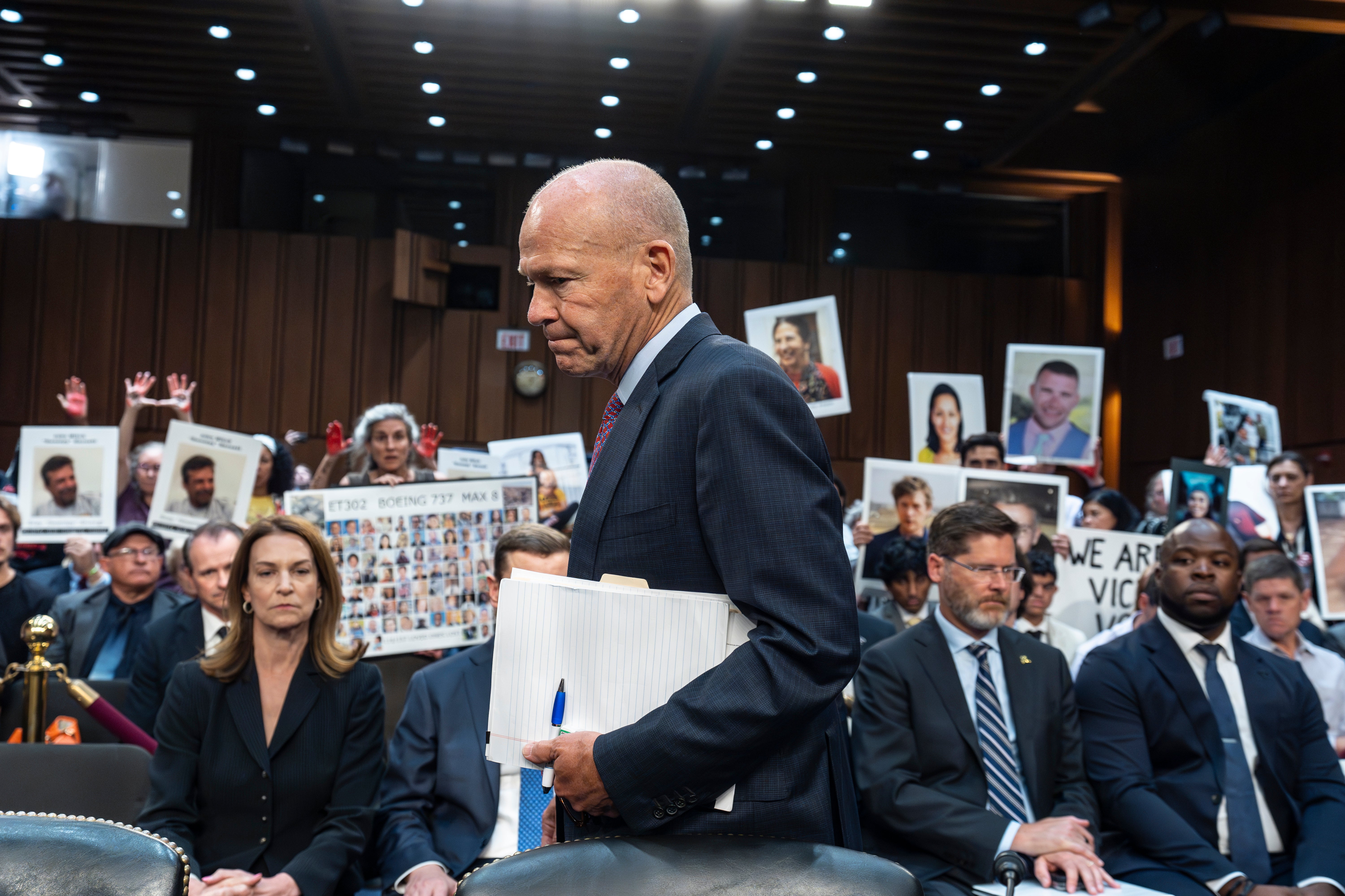 Com os manifestantes na plateia, o CEO da Boeing, Dave Calhoun, chega a uma audiência do subcomitê do Senado para responder aos legisladores sobre os problemas da fabricante de aeronaves.  Ike Riffel, um pai californiano cujos dois filhos morreram em 2019 quando um jato Boeing 737 Max caiu na Etiópia