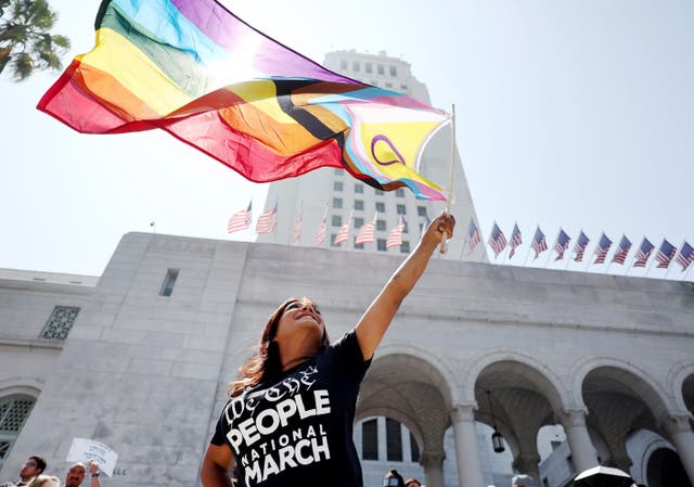 <p>A protester waves a Pride flag incorporating the purple circle emblem of the intersex rights movement outside the Los Angeles city hall in July 2023</p>