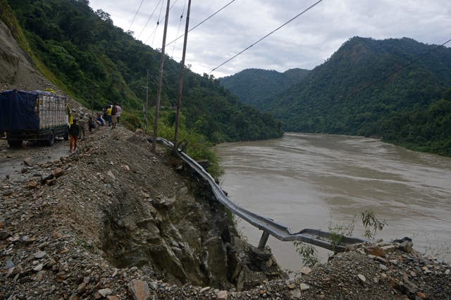 <p>Workers stand at the site of a landslide along the national highway following heavy rains in Setijhora, some 40 kms from Siliguri on October 20, 2021</p>