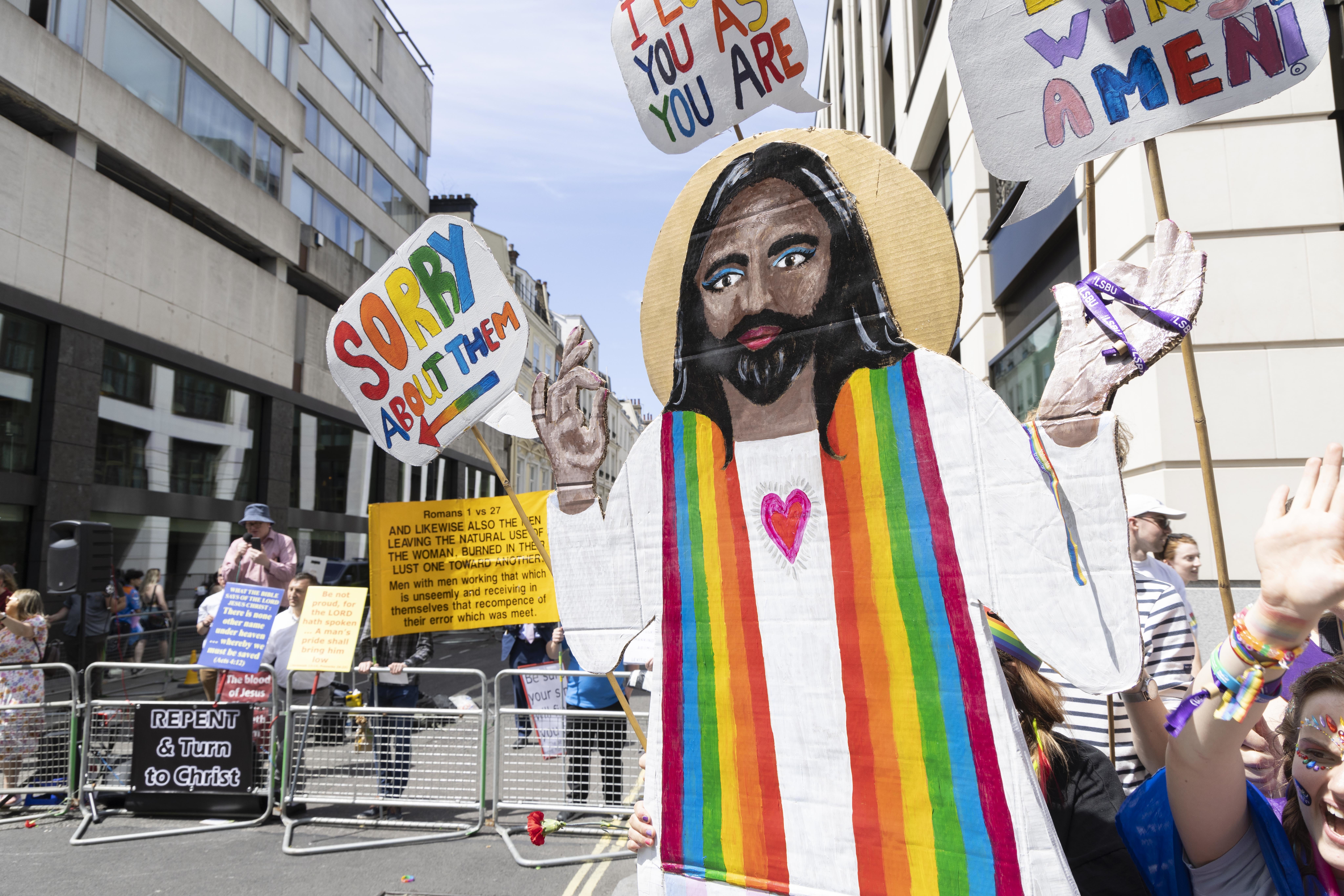 A cardboard figure of Jesus Christ holds a sign, ‘I’m sorry about them’, pointing toward Christian protesters