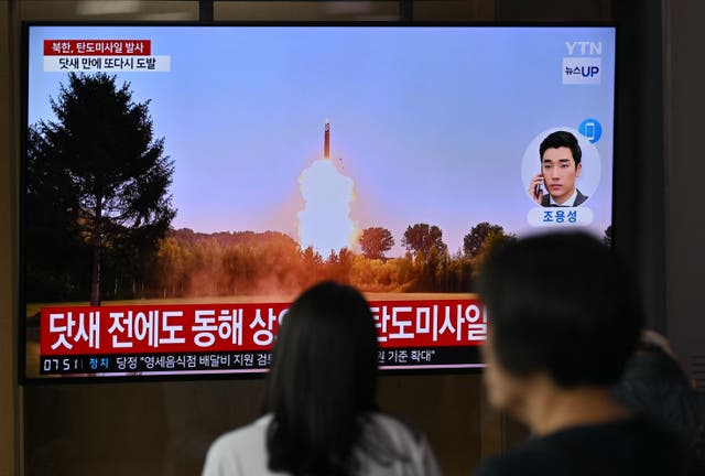 <p>People watch a television screen showing a news broadcast with file footage of a North Korean missile test</p>