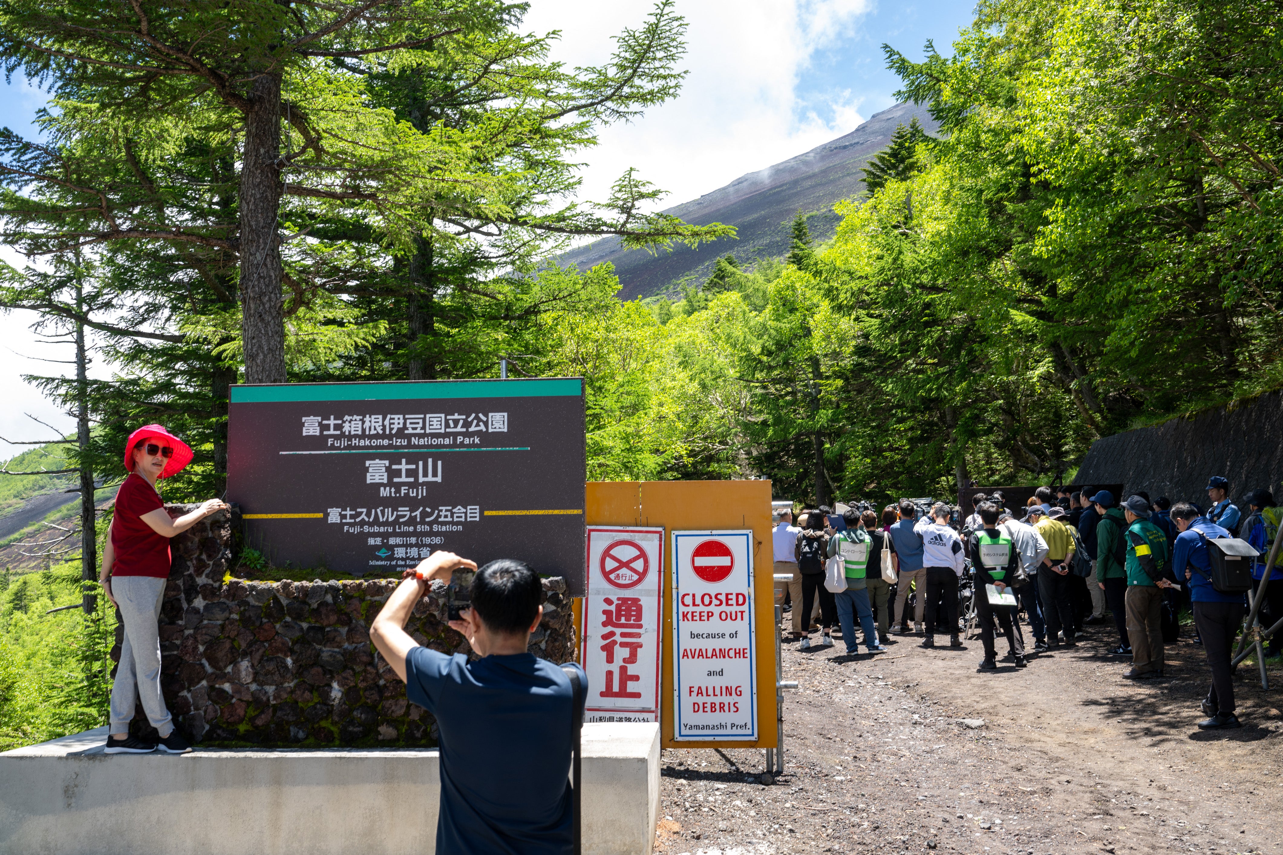 A tourist poses in front of the gate of a national park near the Fuji Subaru Line 5th station, which leads to the Yoshida trail for hikers climbing Mount Fuji