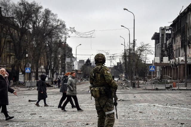 <p>People pass by a Russian soldier in central Mariupol</p>