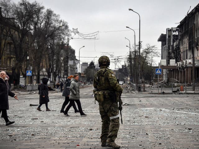 <p>People pass by a Russian soldier in central Mariupol</p>