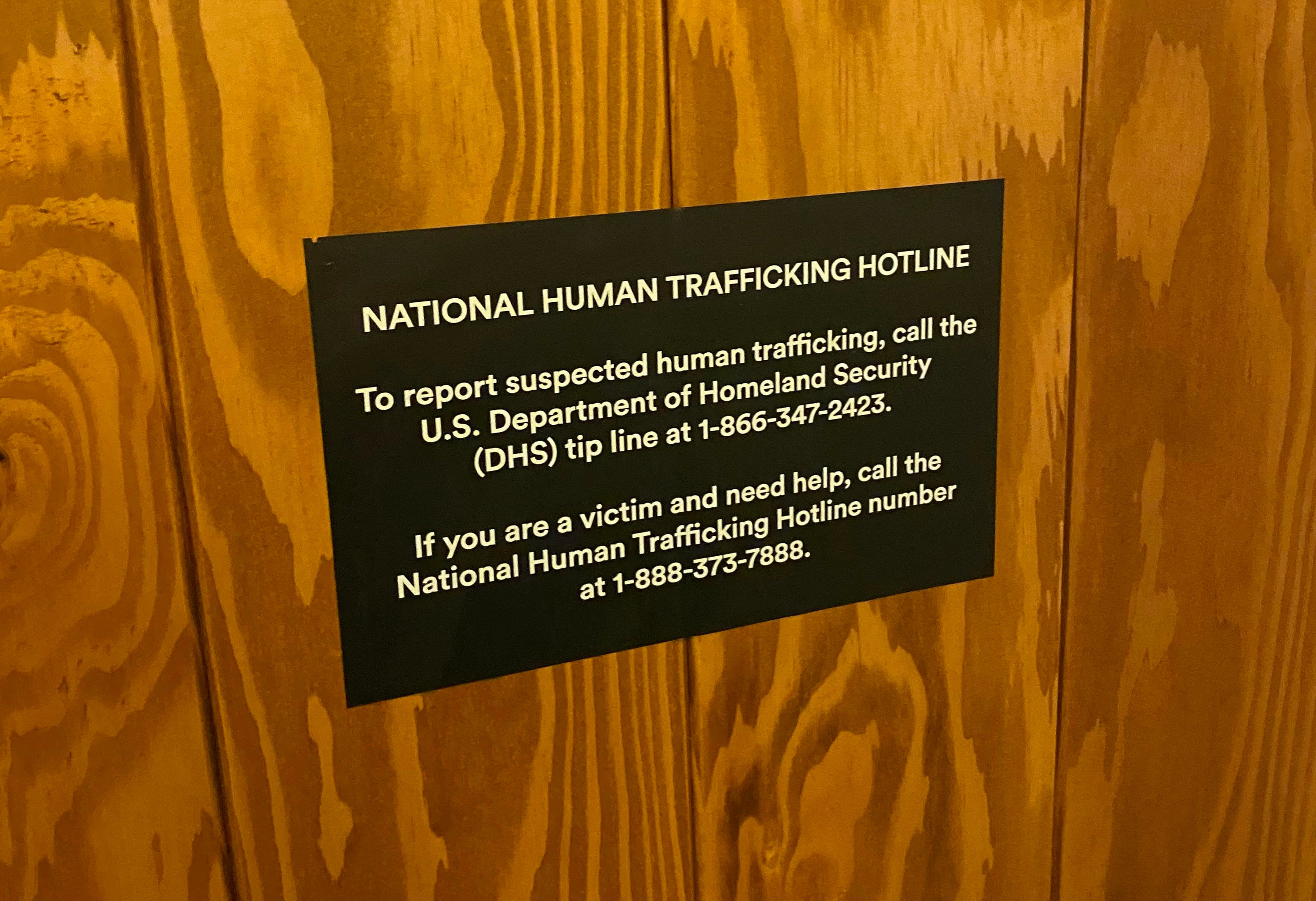 A sign displaying the phone number for the National Human Trafficking Hotline on the back of a door at a New York City hotel.