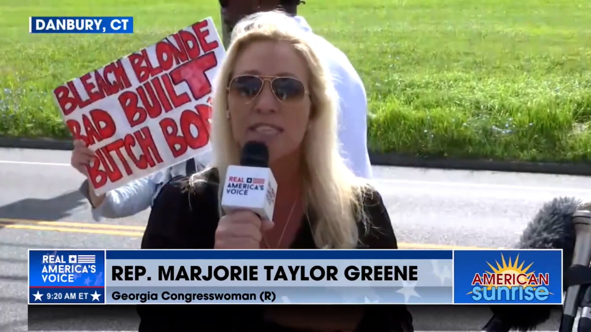Majorie Taylor Greene speaks outside a Danbury, Connecticut, prison as Steve Bannon turns himself in. A protestor held up a sign mocking the Georgia representative during her TV appearance