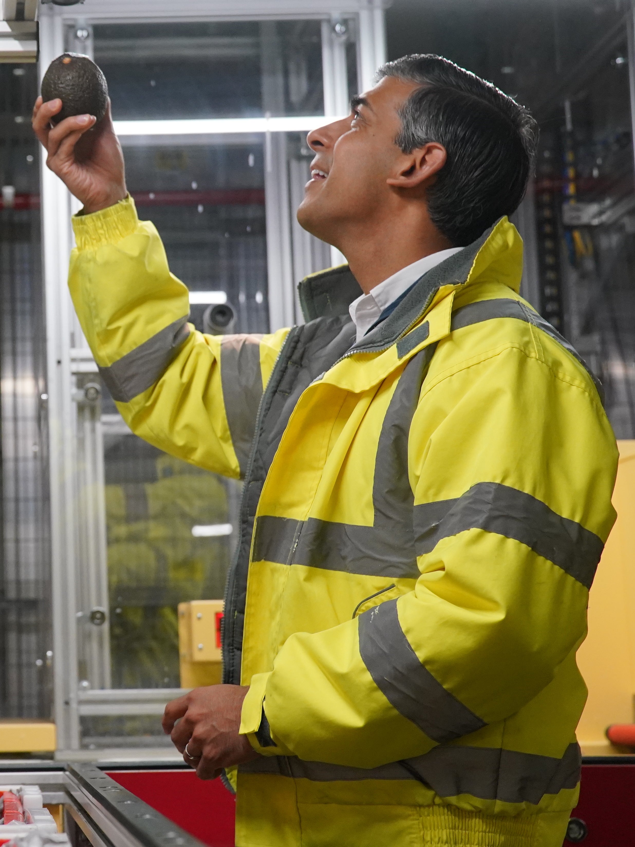 Rishi Sunak inspects an avocado during a campaign visit to an Ocado distribution warehouse in Luton (Jonathan Brady/PA)