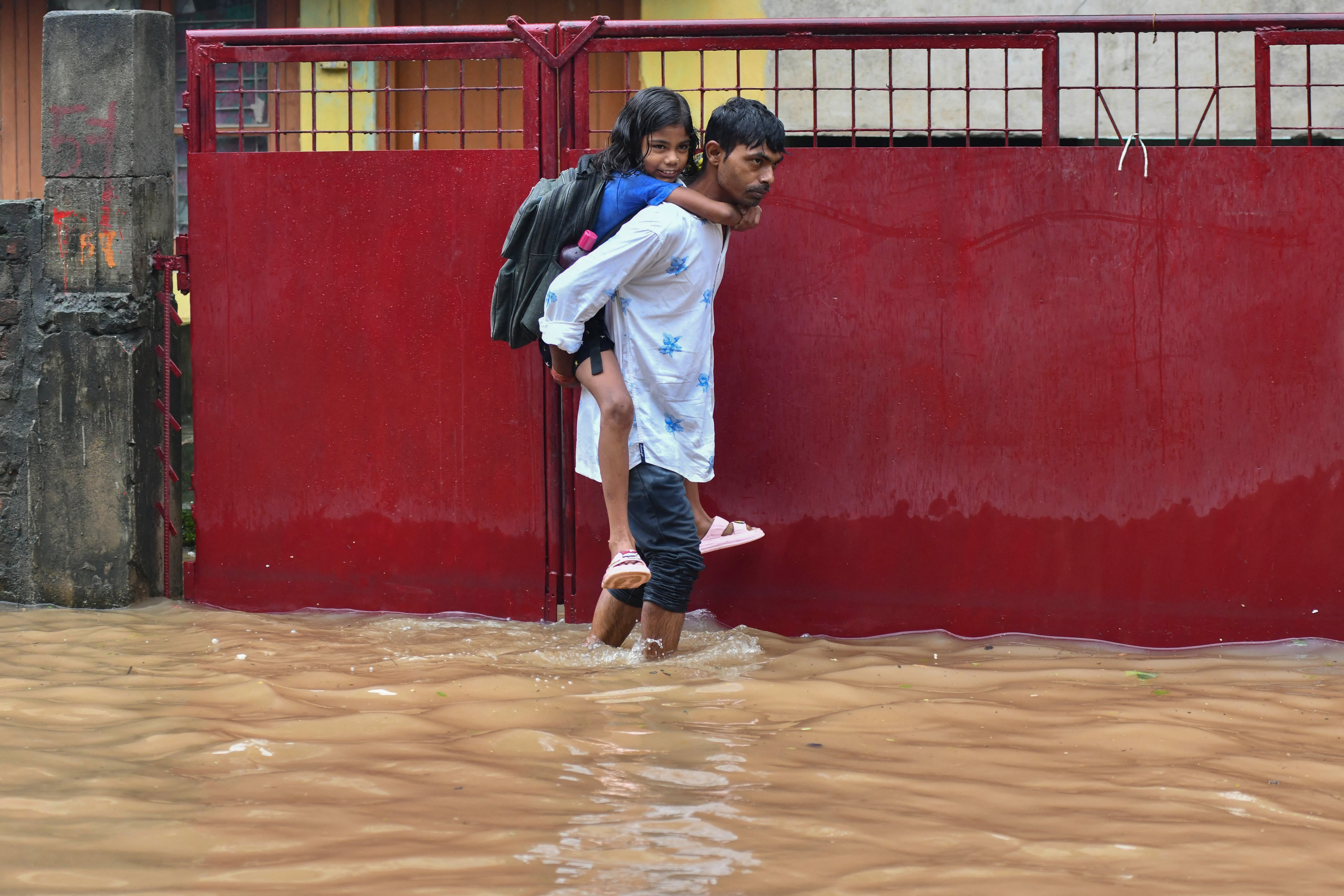 A man carries his daughter on back as he wades through a flooded street in Guwahati on June 20