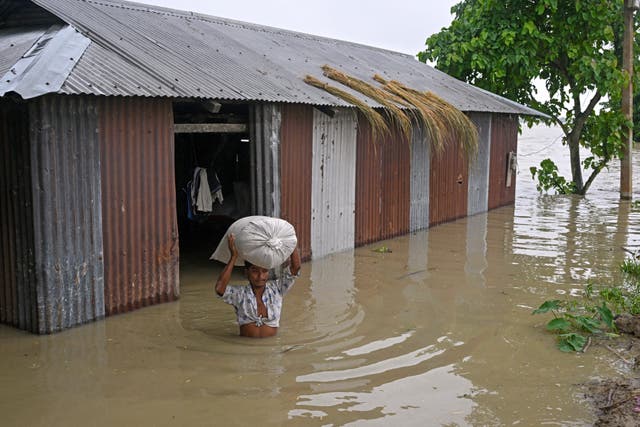 <p>A man wades across flood waters as he carries a sack of rice from his house deluged by heavy rains at Morigaon district in Assam</p>