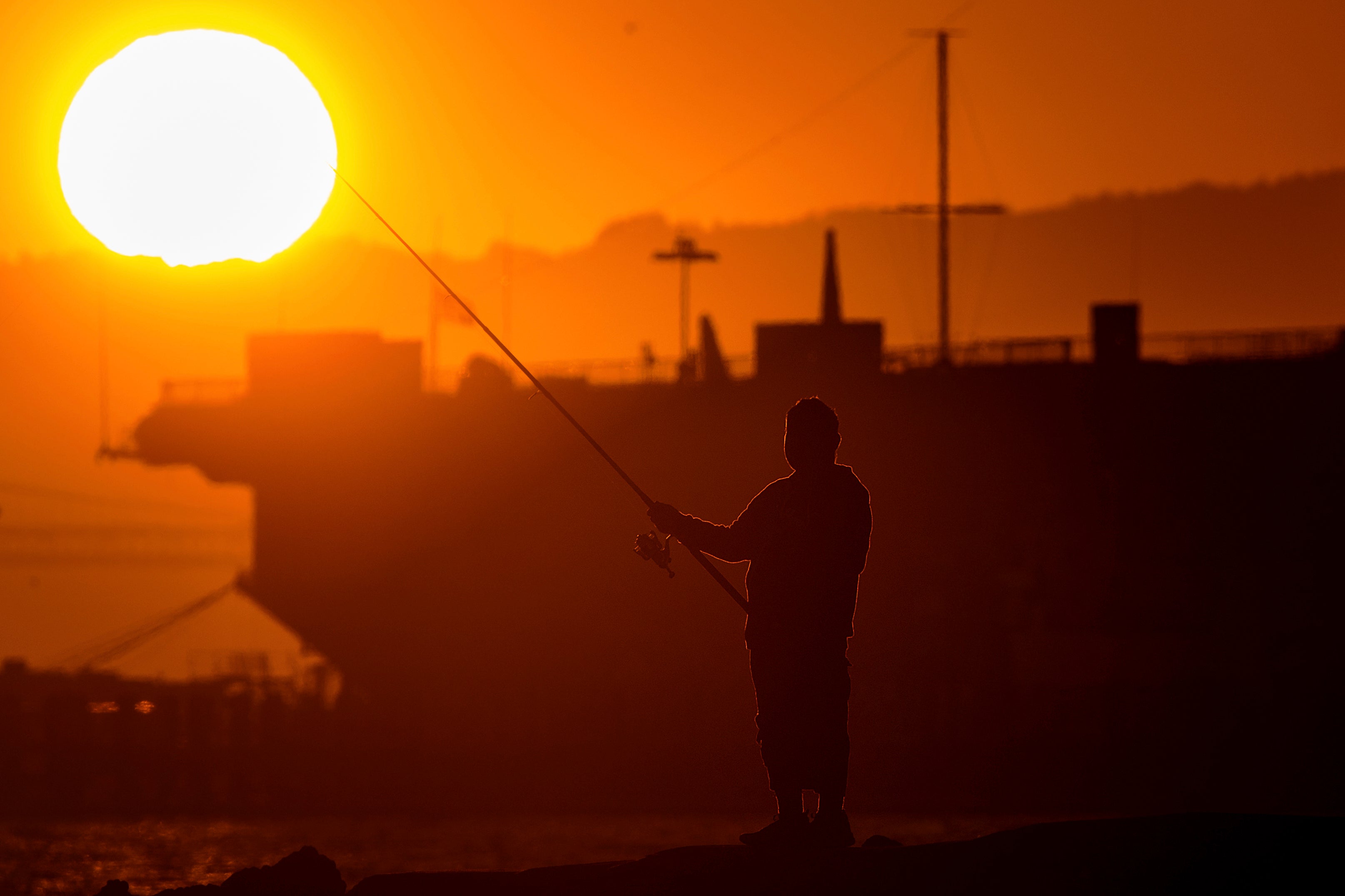 A man fishes off a jetty in Alameda, California, as the sun sets over the San Francisco Bay on July 1. An extended heatwave predicted to blanket Northern California has resulted in red flag fire warnings and the possibility of power shutoffs beginning Tuesday