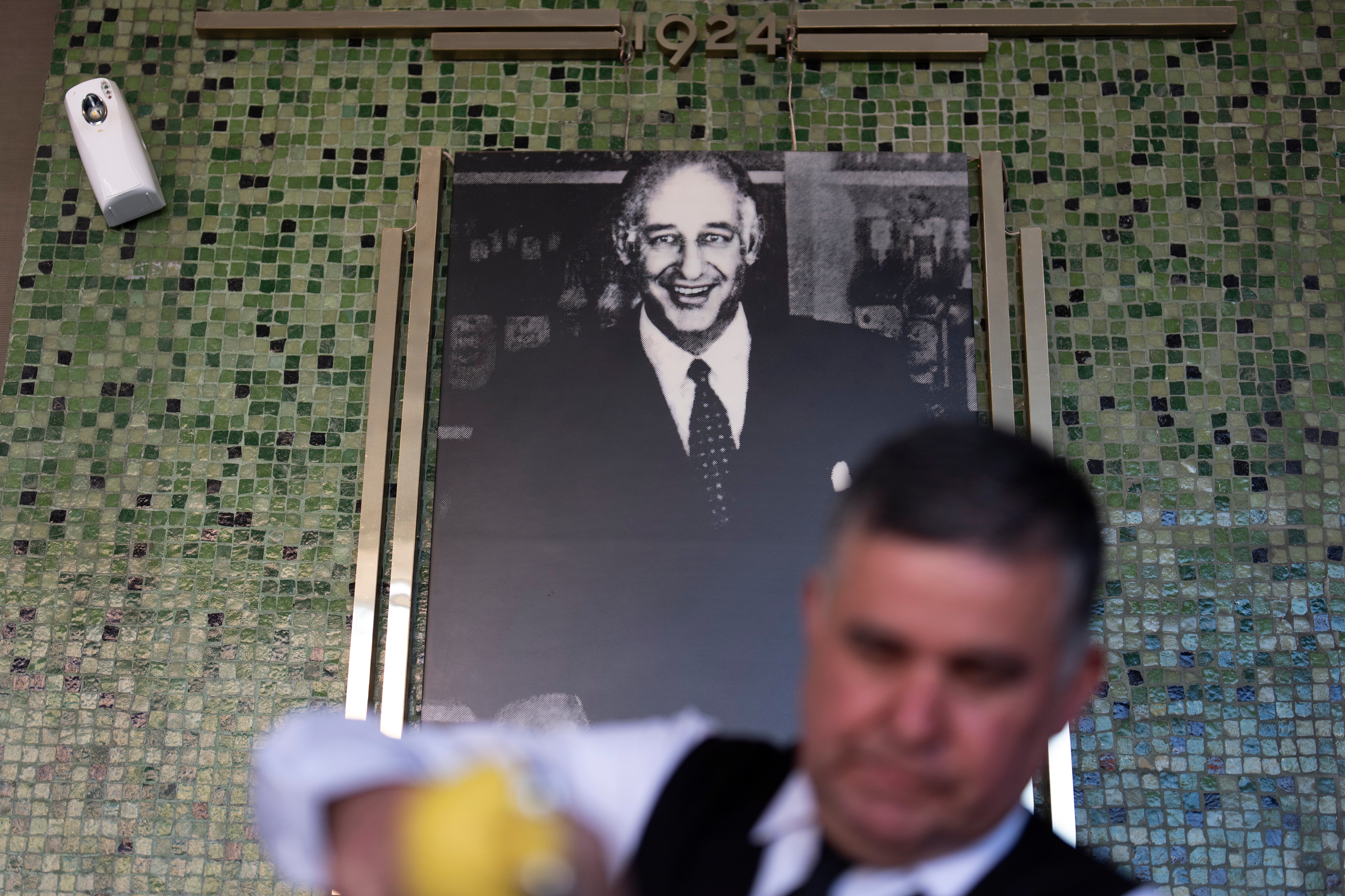 Salad Master Efrain Montoya prepares a Caesar salad in front of an image of the said inventor of the salad, Caesar Cardini