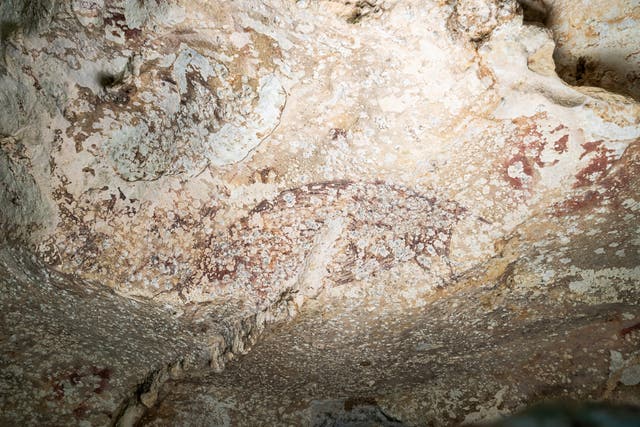 <p>A painting created at least 51,200 years ago in the limestone cave of Leang Karampuang in the Maros-Pangkep region of the Indonesian island of Sulawesi portrays three human-like figures interacting with a wild pig</p>