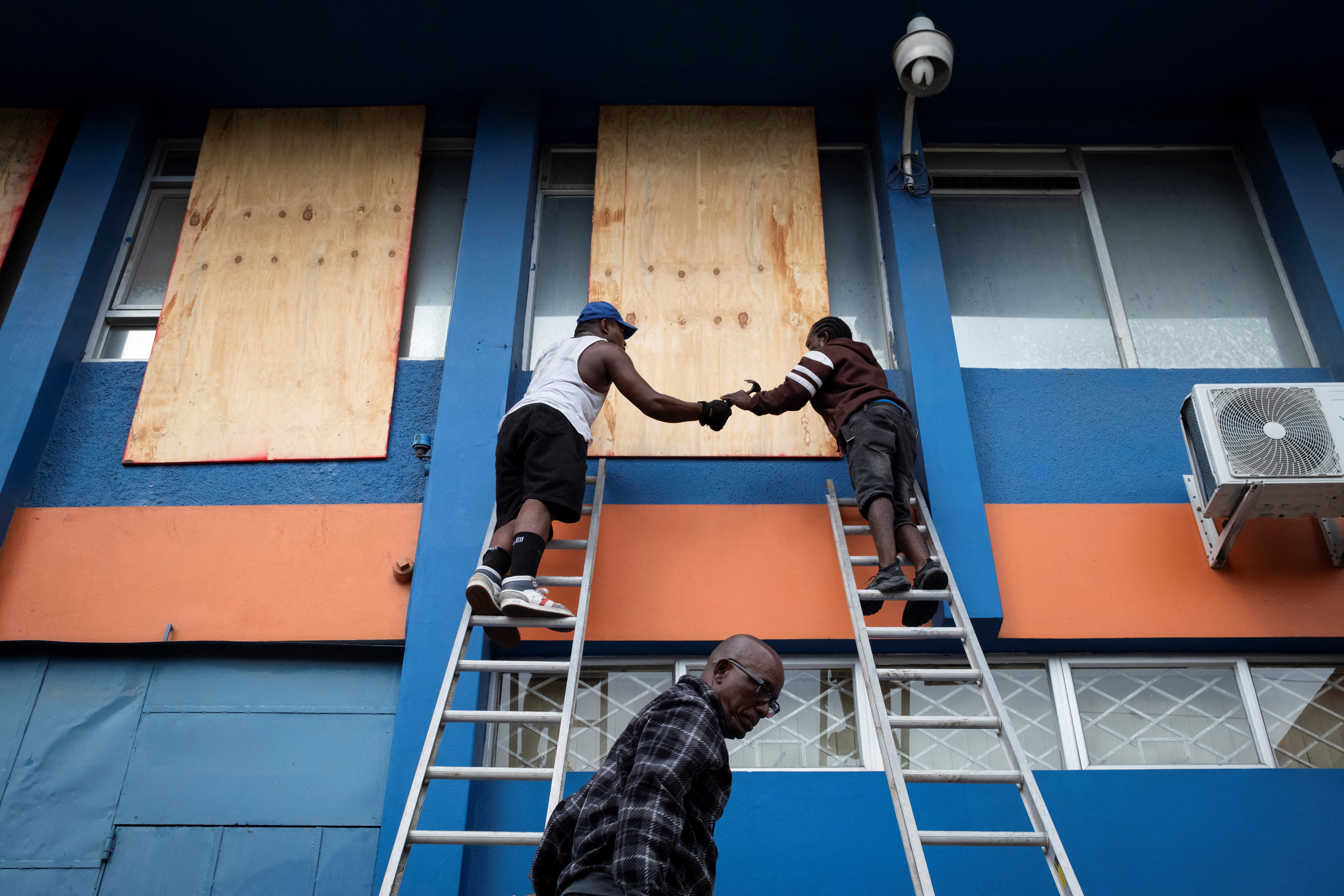 Two people board up the windows of an office building in Kingston, Jamaica on Wednesday as Hurricane Beryl approaches