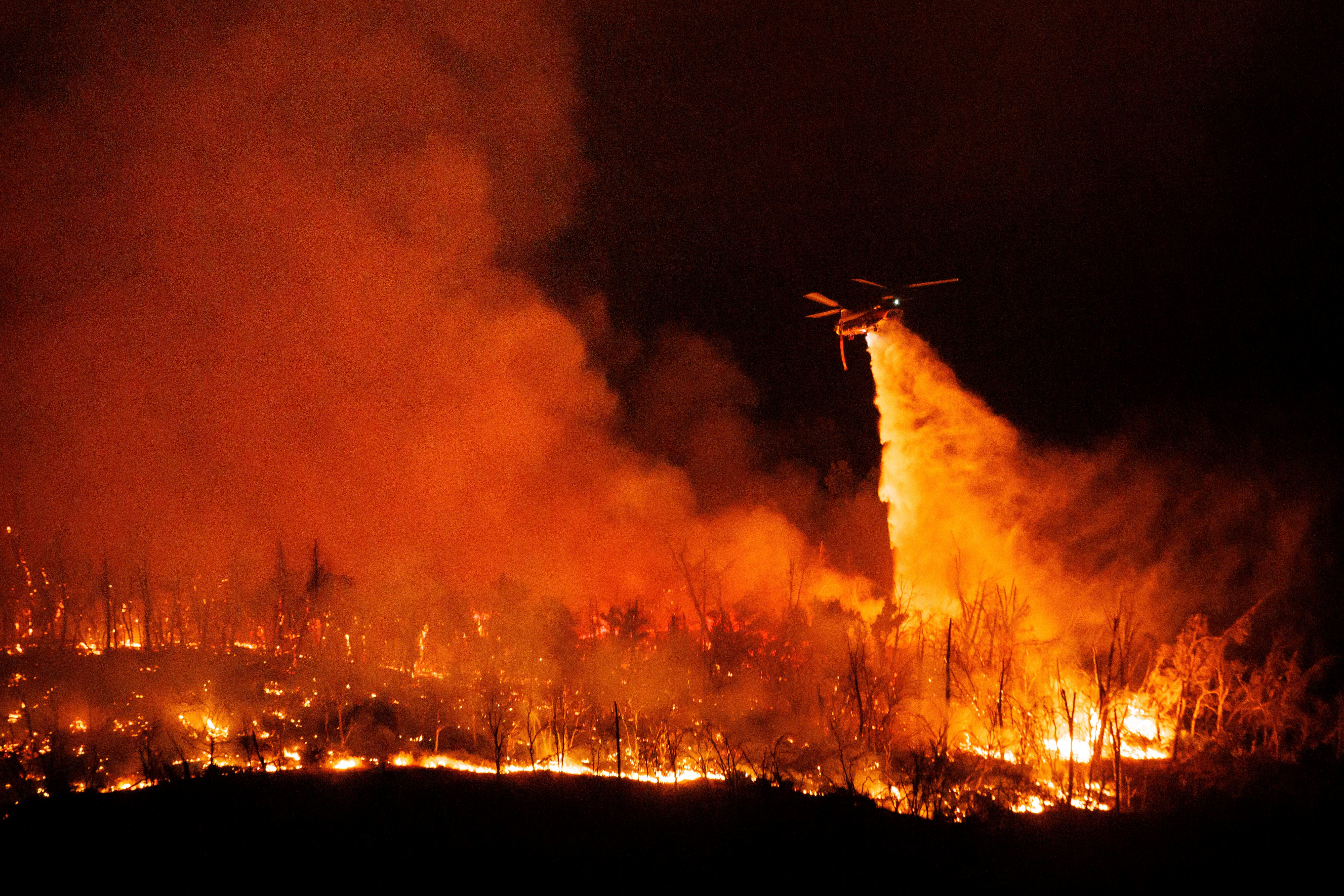 Helicopters try to douse the flames in a forested area of Butte County on Tuesday night