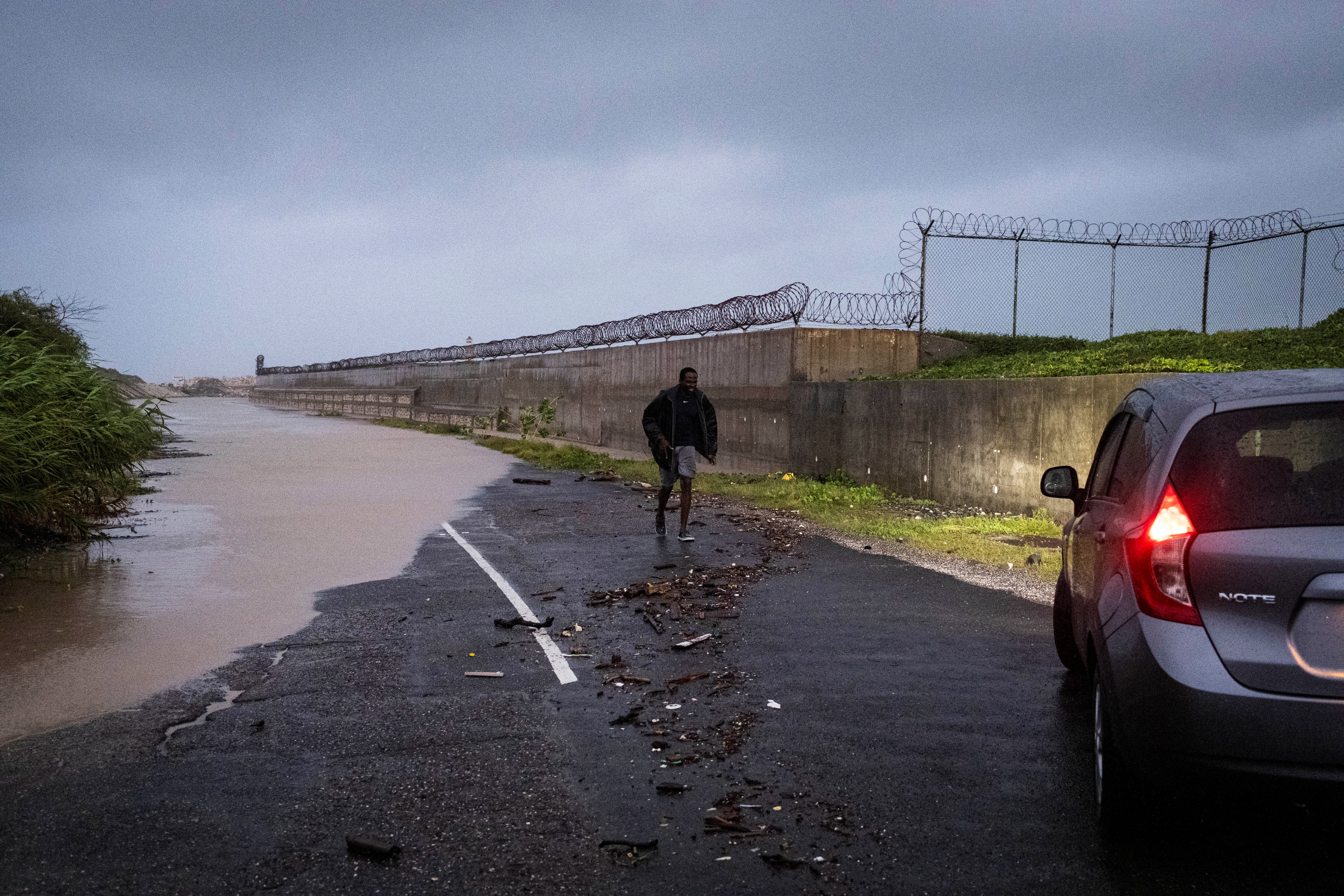 ハリケーン・ベリルがジャマイカ・キングストンの島南部の海岸を襲った後、浸水した道路を評価した後、車で歩いている男